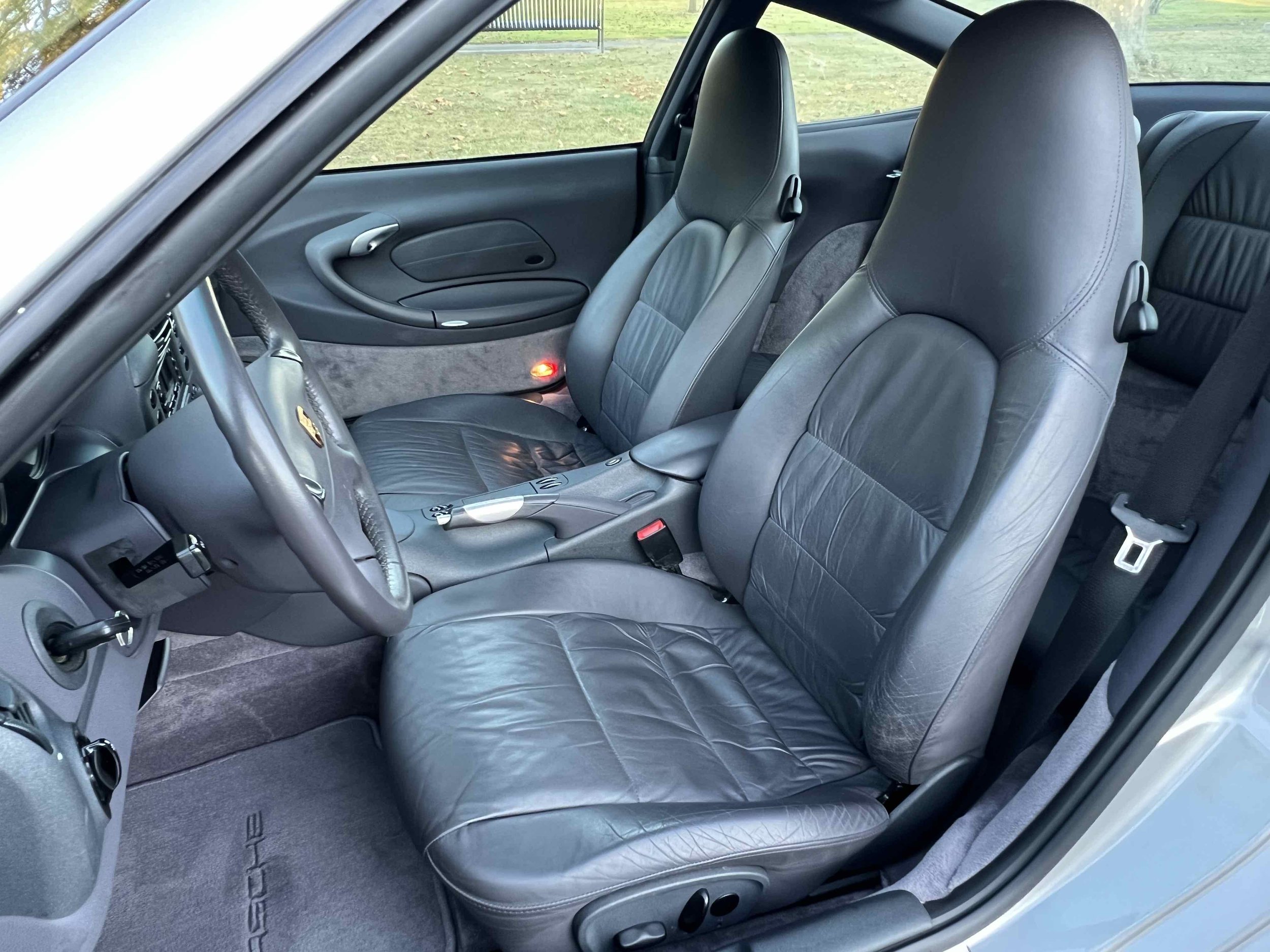 The interior of a sports car with black leather seats, silver console, and gray carpeting.