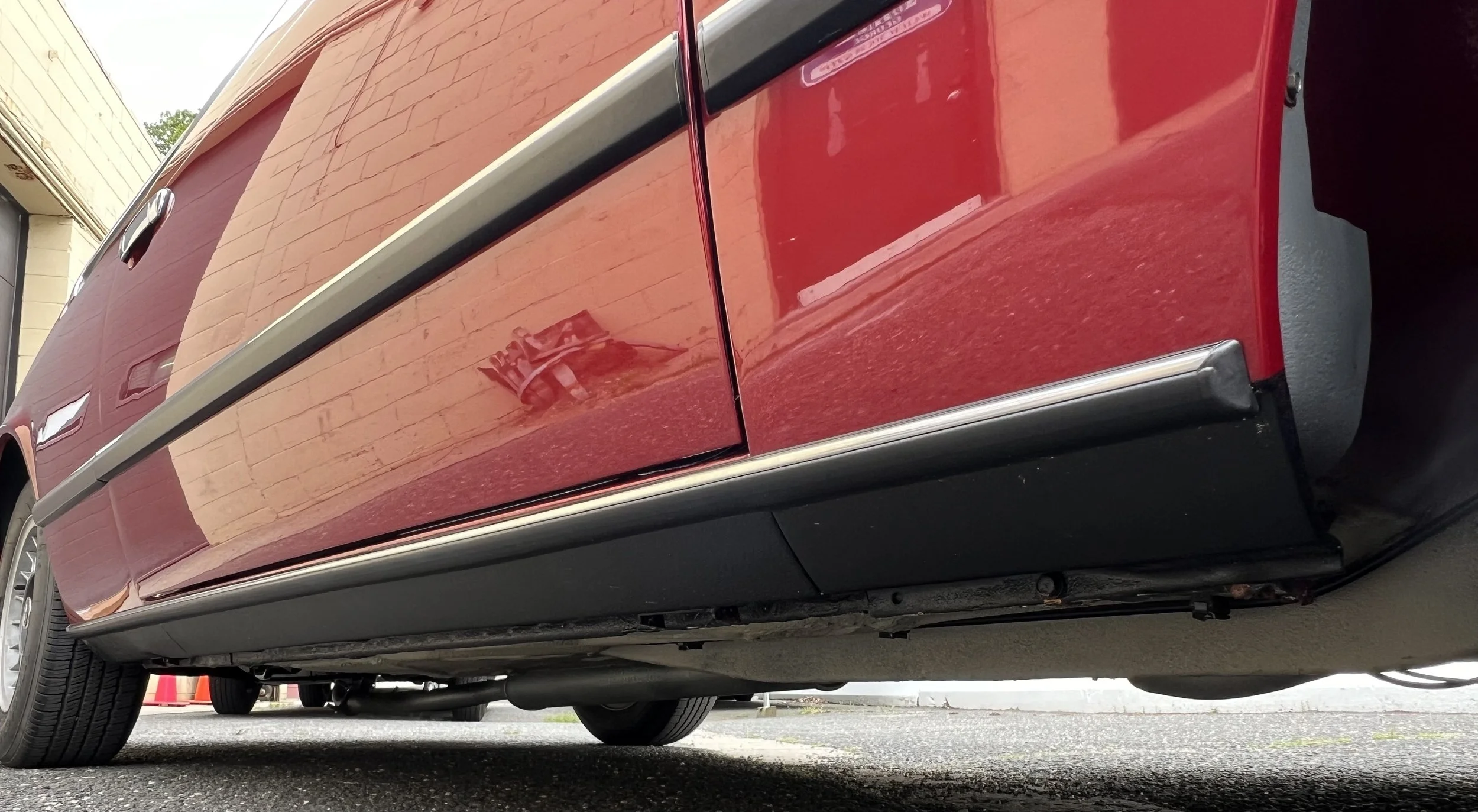 Close-up of the lower side of a red 1977 BMW 630 csi vehicle, showing the side panel, wheel, and part of the undercarriage.