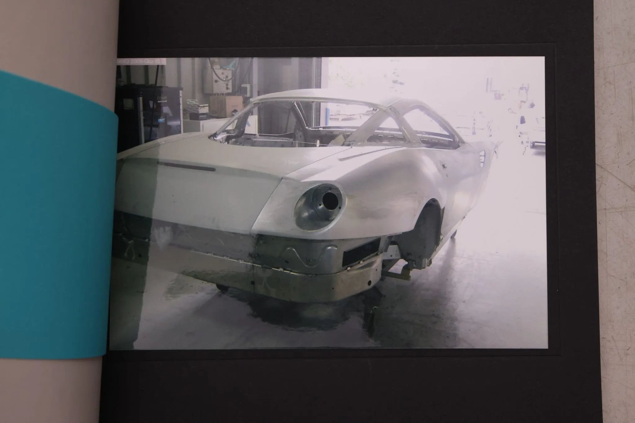 Photo of a vintage race car in a garage with some tools and equipment visible in the background.
