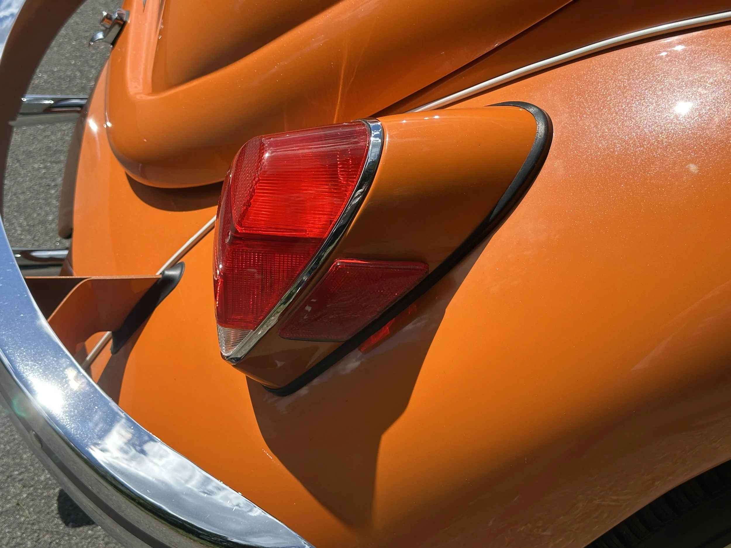 Close-up of the rear part of an orange vintage car, showing the tail light and part of the chrome bumper.