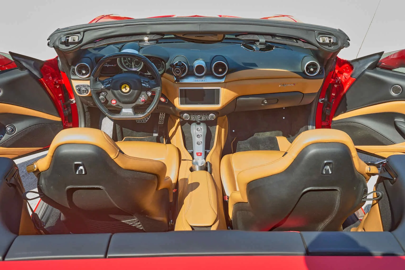 Interior of a yellow Ferrari California convertible, showing the dashboard, steering wheel with Ferrari logo, leather seats, and center console.