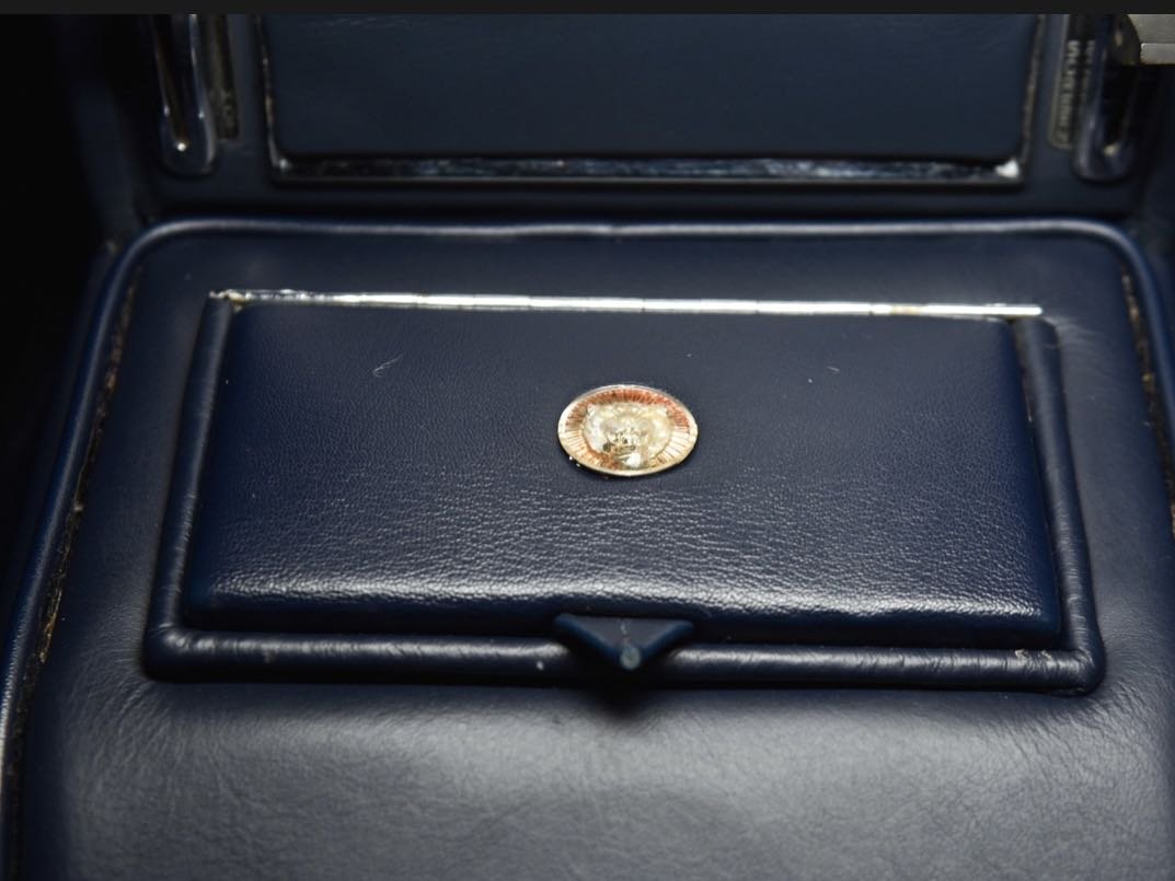A coin placed on a dark blue leather surface inside a vehicle, possibly a car's center console or armrest area.