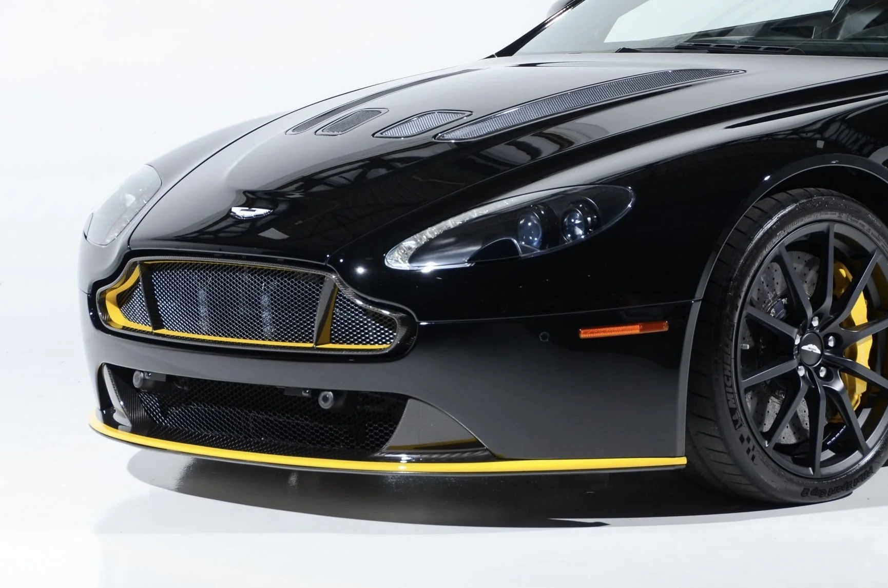 Close-up of a black sports car with yellow accents, showing the front grille, headlight, and front wheel.