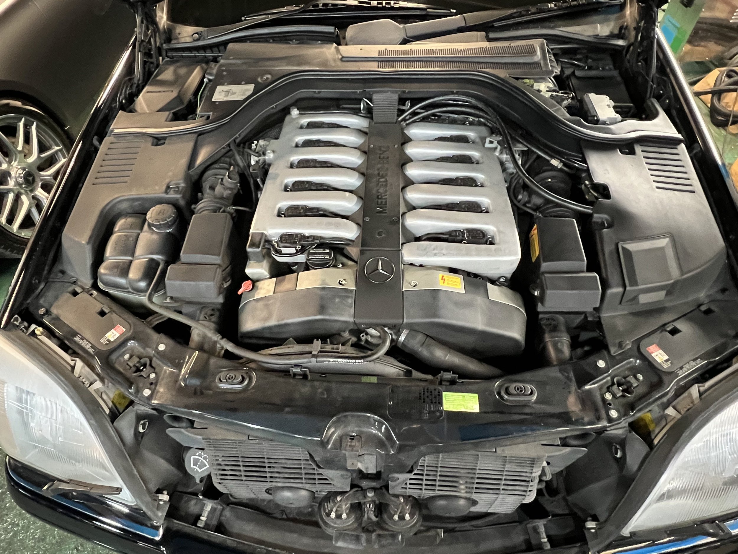 Open hood of a Mercedes-Benz car revealing the engine bay with a Mercedes-Benz V8 engine.