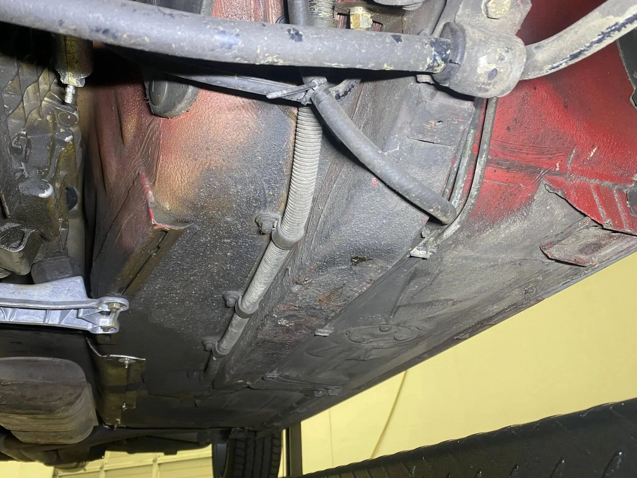 Underneath view of a vehicle's chassis showing parts of the suspension and drivetrain, with signs of oil and dirt accumulation.