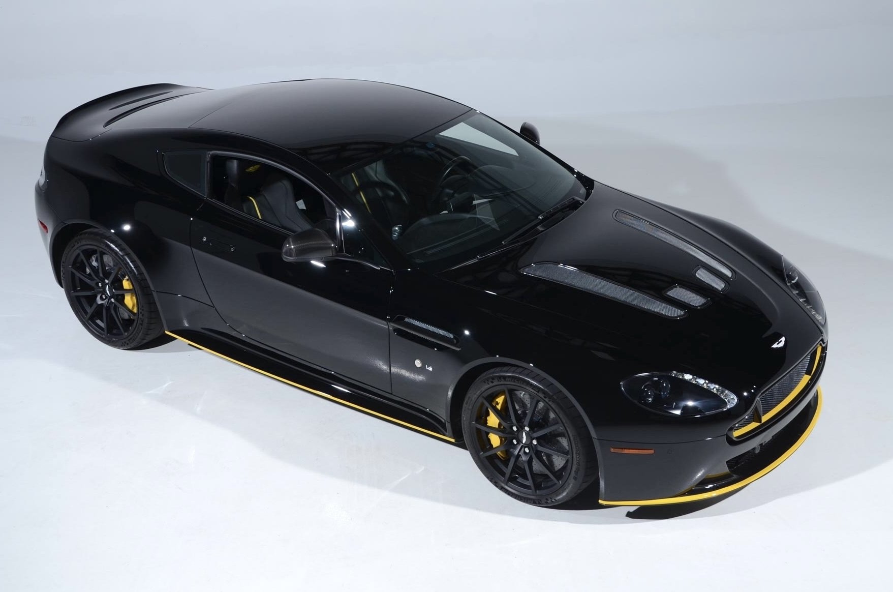 A sleek black sports car with yellow accents and black wheels parked on a white surface.