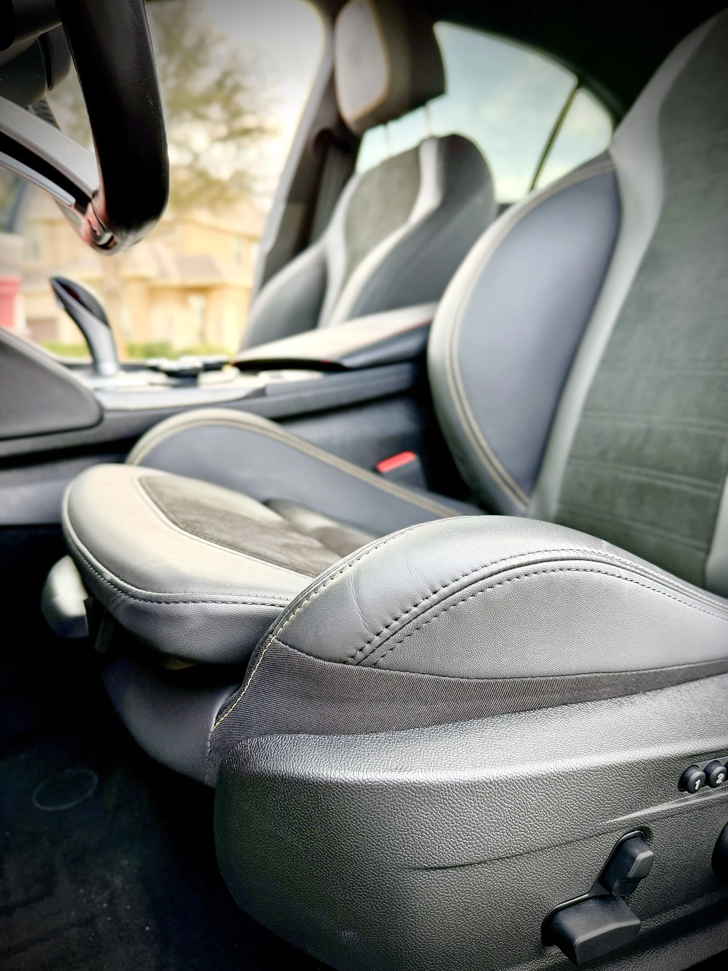 Close-up of front passenger seat in a car interior, with gray fabric and leather upholstery, showing the seat adjustment controls.
