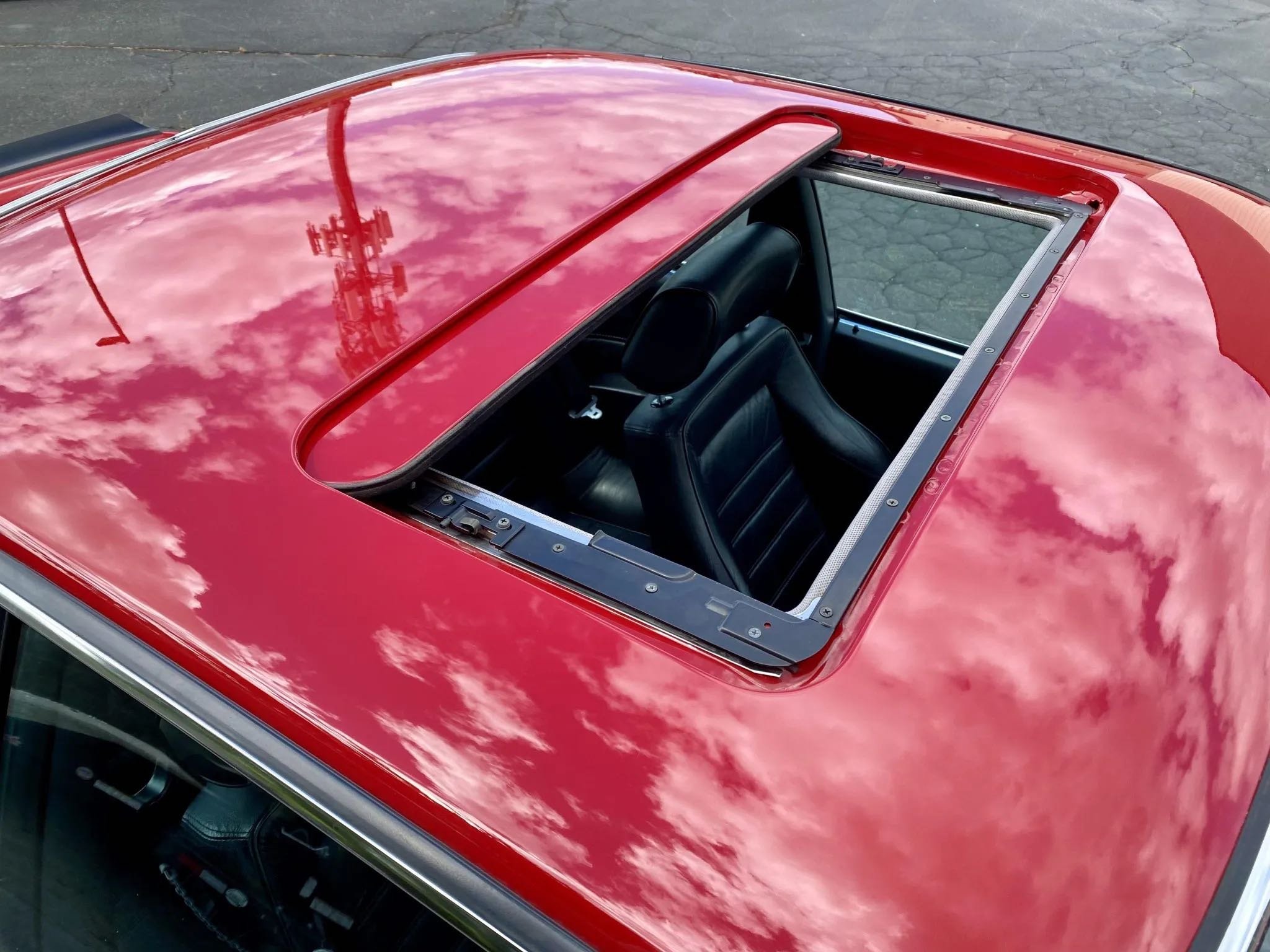Red car with a sunroof opened, showing black leather interior and headrests on the seats, reflecting a cloudy sky.