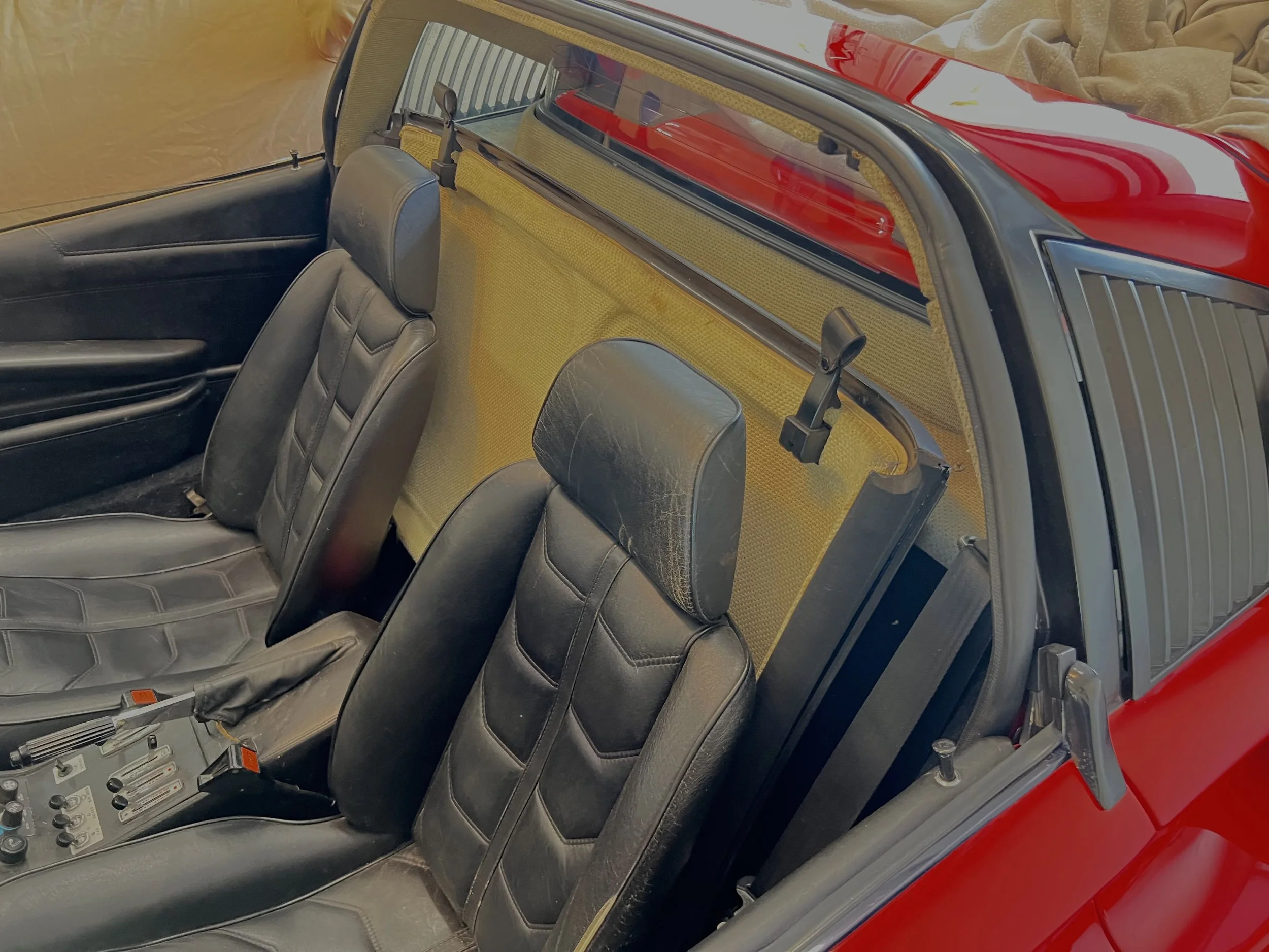 The interior of a classic red car showing two black leather seats, a dashboard with controls, and a yellow partition behind the seats.