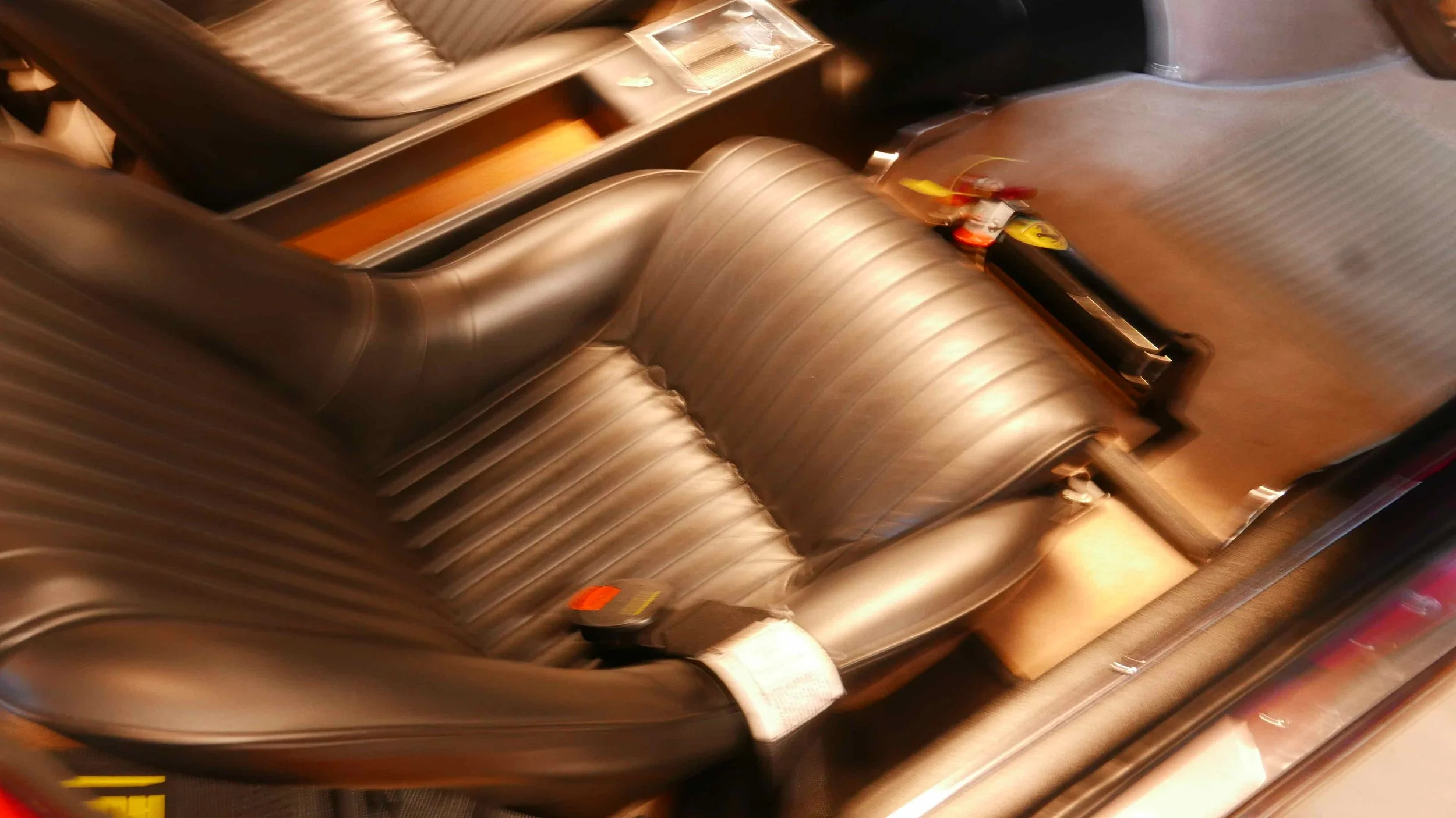 Leather Ferrari seat with adjustable headrest and armrest, and a small holder on the side.