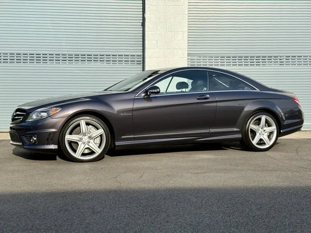 Driver side of Grey 2008 Mercedes Benz CL63 AMG on pavement with two green garage doors in the background for sale at FlowHaus