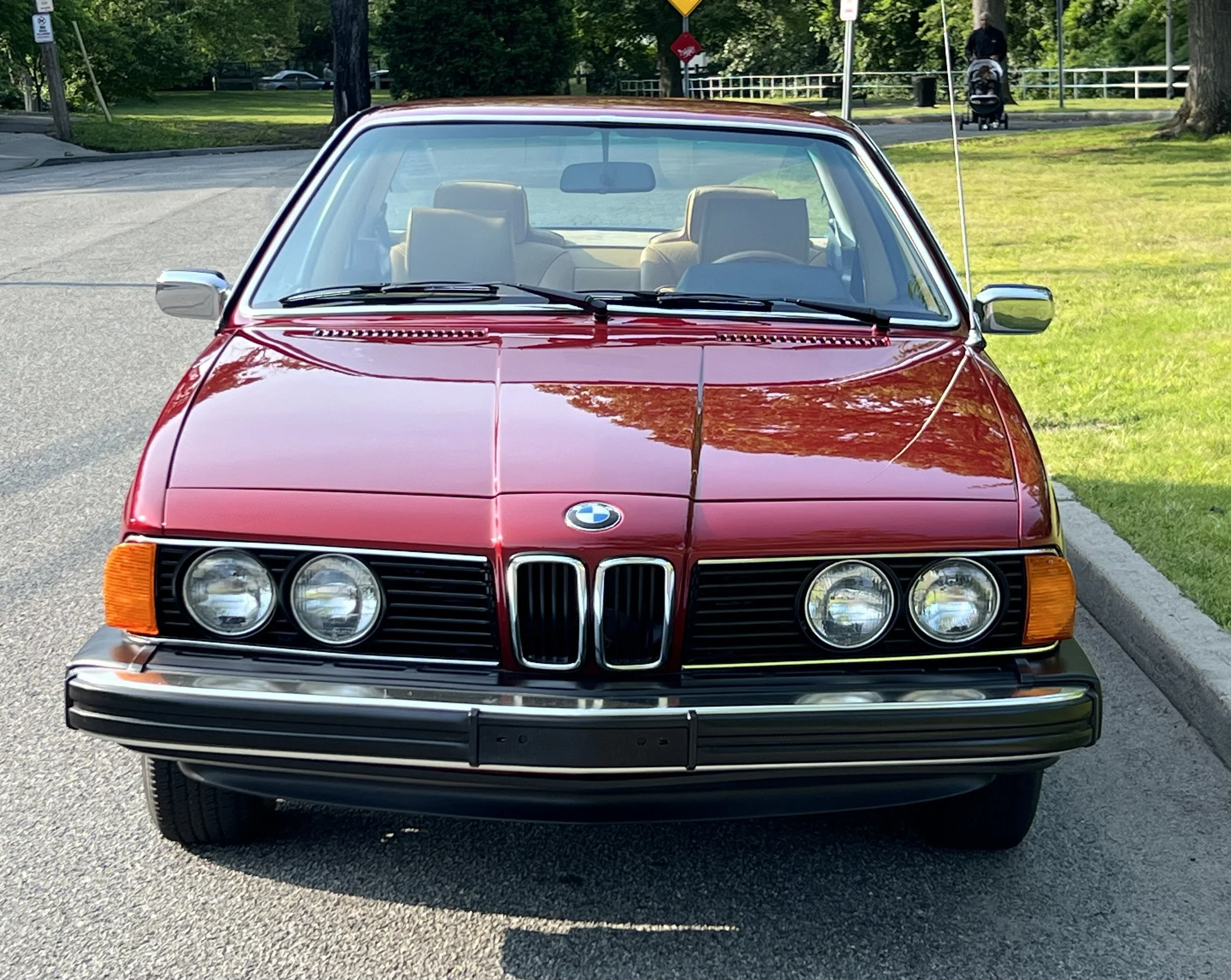 Front of Ruby Red 1977 BMW 630 csi on display in park with trees and grass in background for sale at FlowHaus