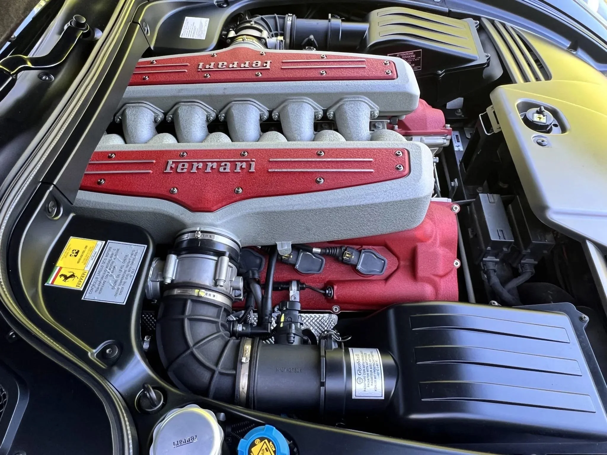 Close-up of a Ferrari engine with red valve covers and silver intake manifold, placed inside a car engine bay.