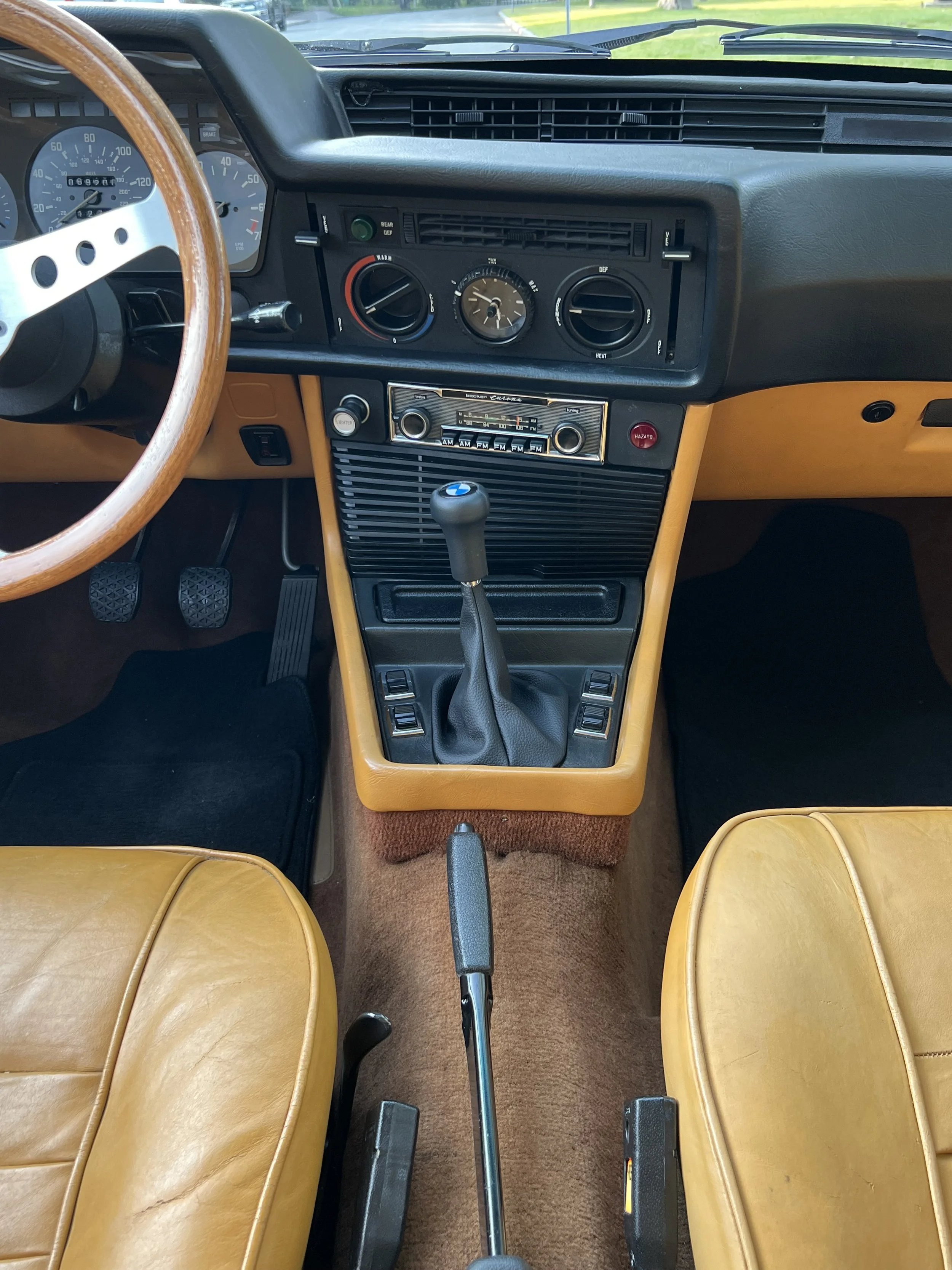 Interior of a vintage BMW BMW 630 csi car, showing the dashboard with a speedometer, radio, gear shift, and tan leather seats.
