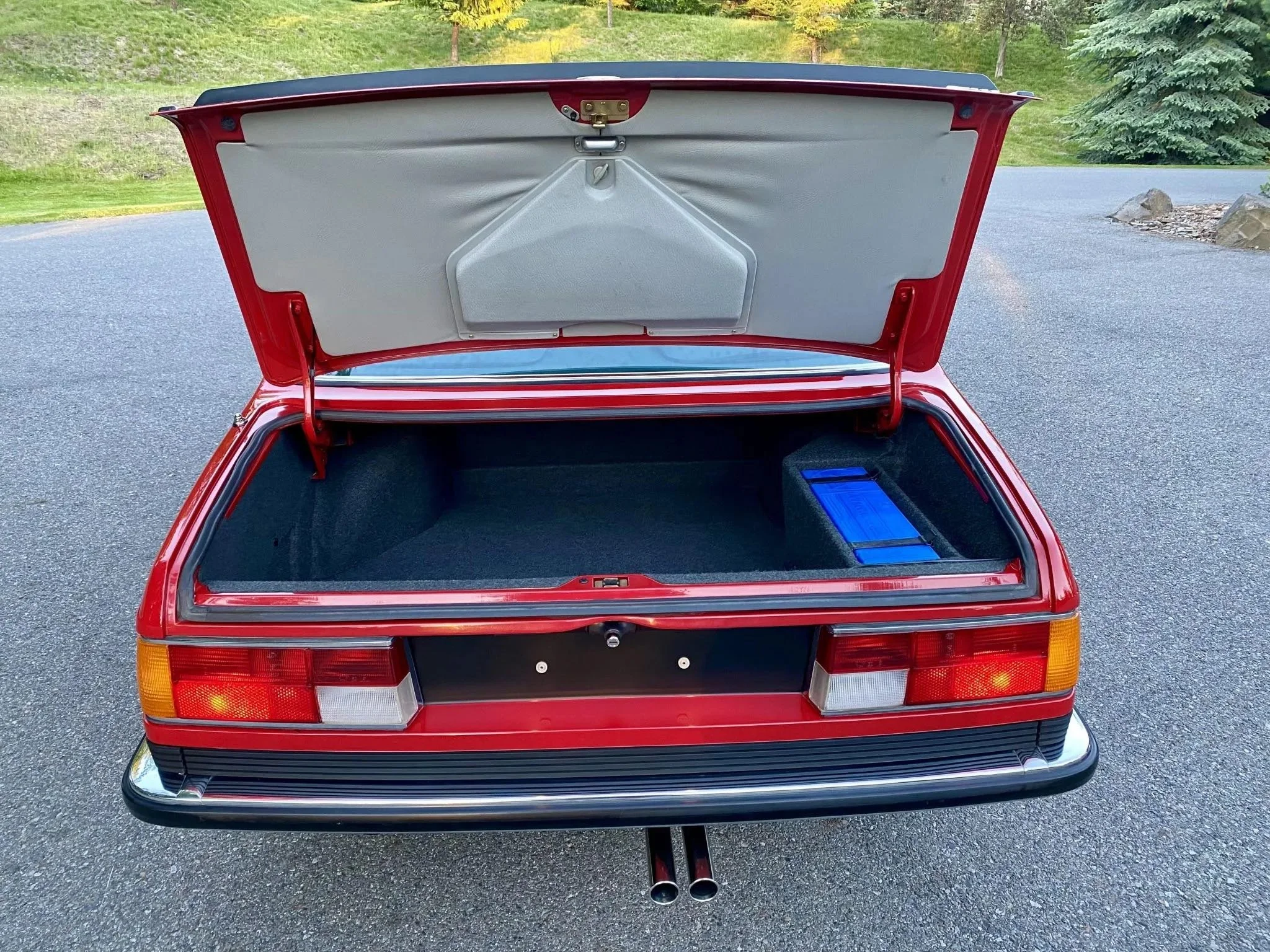 Open red car trunk showing empty interior with a blue rectangular object on the right side inside the trunk.