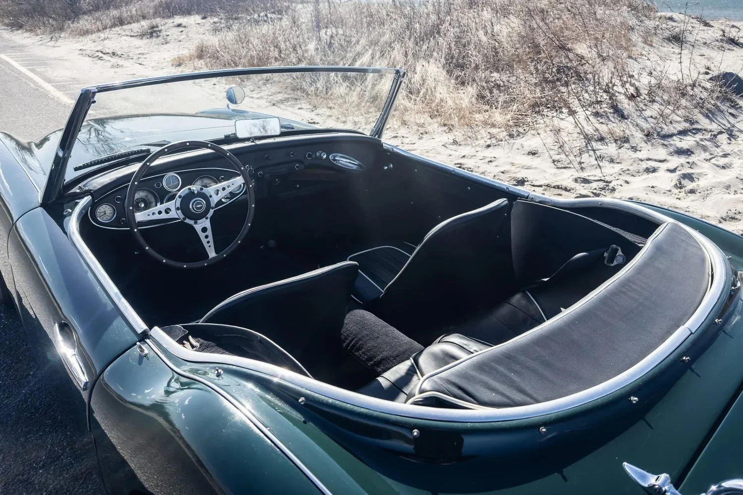 Interior of a vintage convertible car parked on a sandy roadside with dry grass in the background.