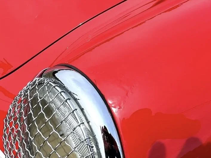Close-up of the front part of a red car, focusing on the headlight and chrome grille.