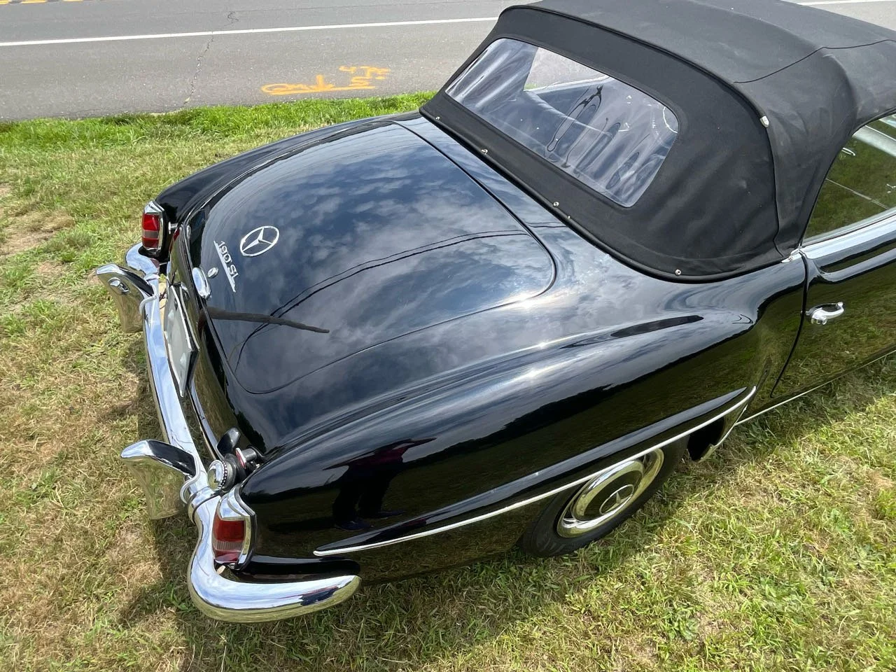 A vintage black Mercedes-Benz with a soft top, parked on grass near a road.