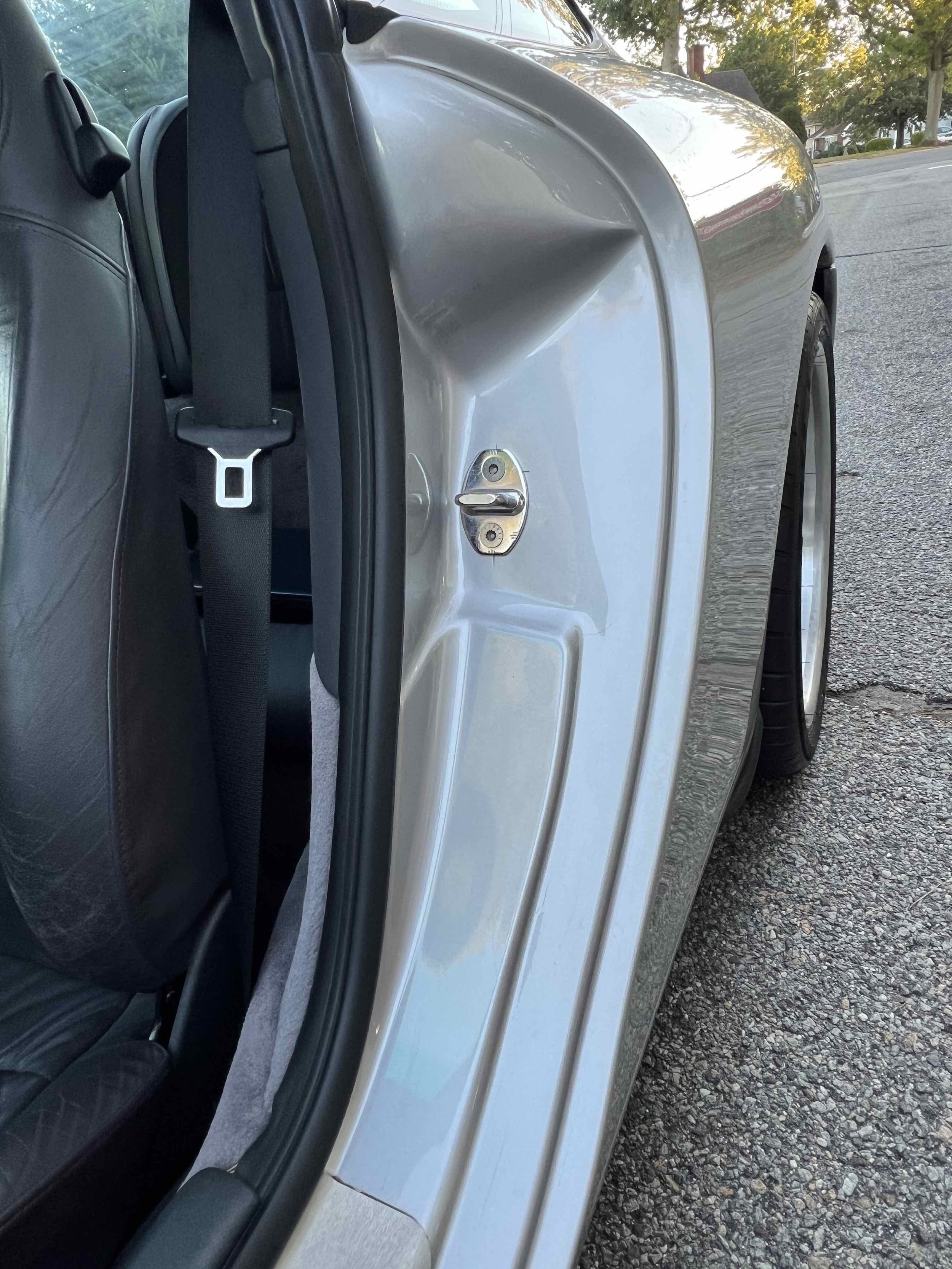 Close-up of a silver car door with the latch and lock mechanism visible, showing the interior and part of the rear seat with a seatbelt.