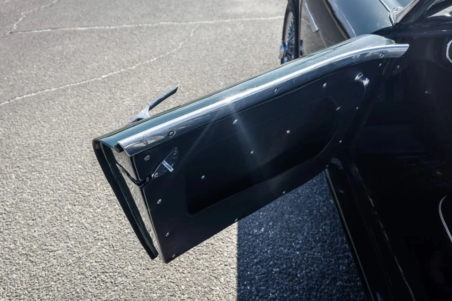 Close-up of an open vintage black car door with metal trim on a paved surface.