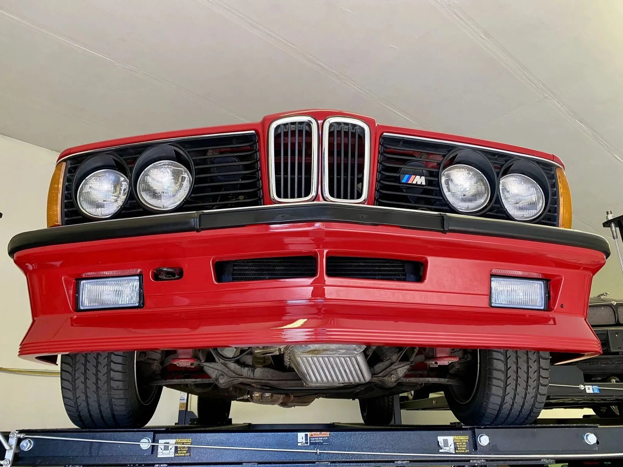 Front view of a red BMW car with black grille and round headlights, mounted on a lift in a garage.