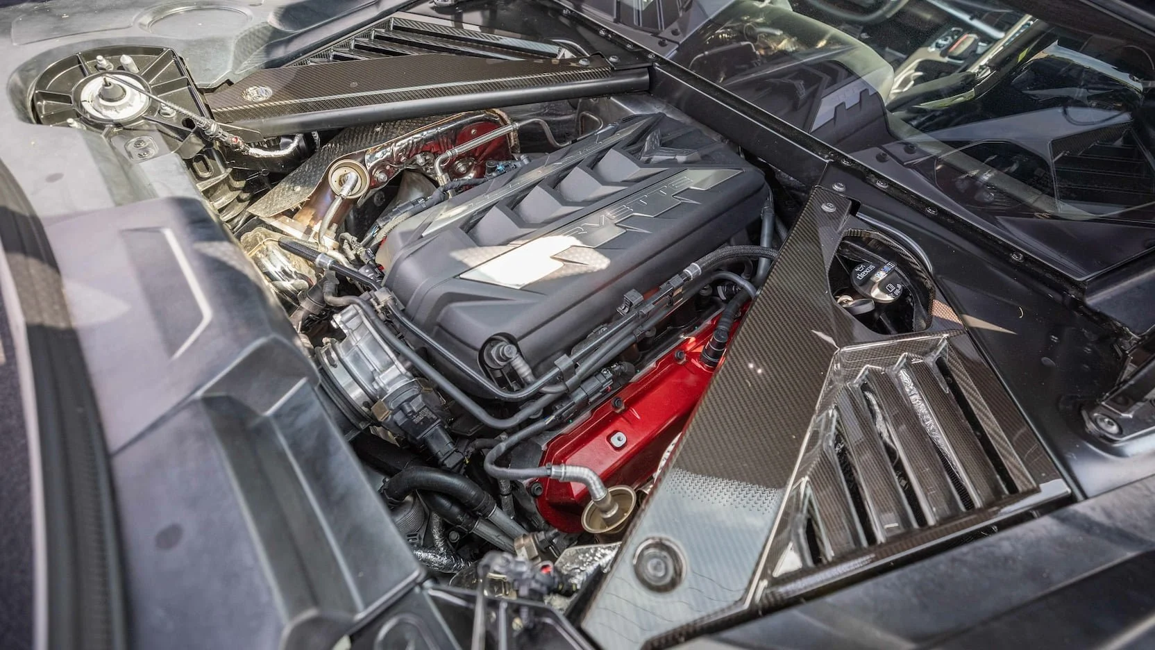Close-up of a high-performance car engine, featuring a ribbed black cover with the word 'Corvette' and to the side a red engine block.