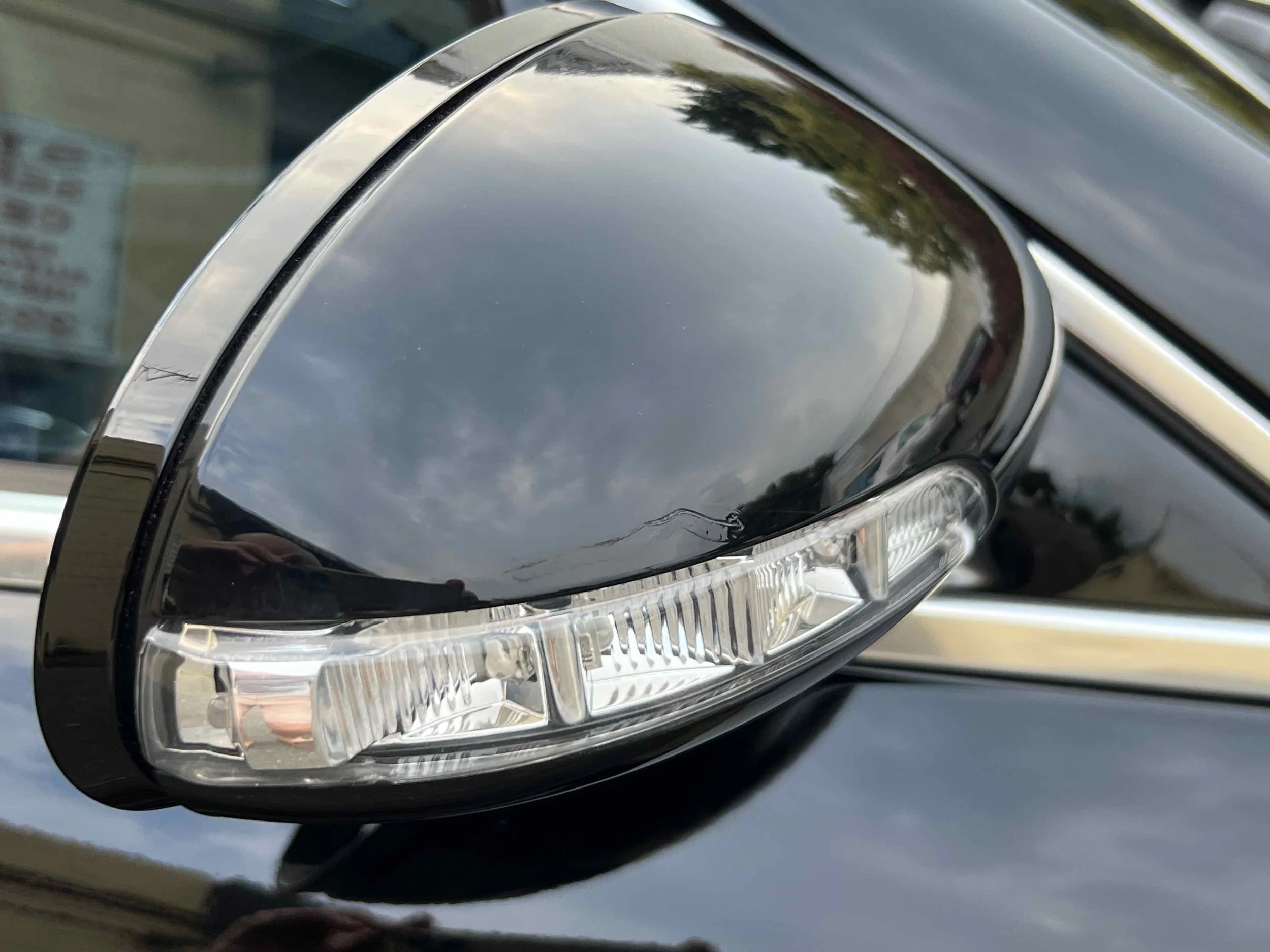 Close-up of a black car's side mirror with a reflective surface showing the cloudy sky and surroundings.