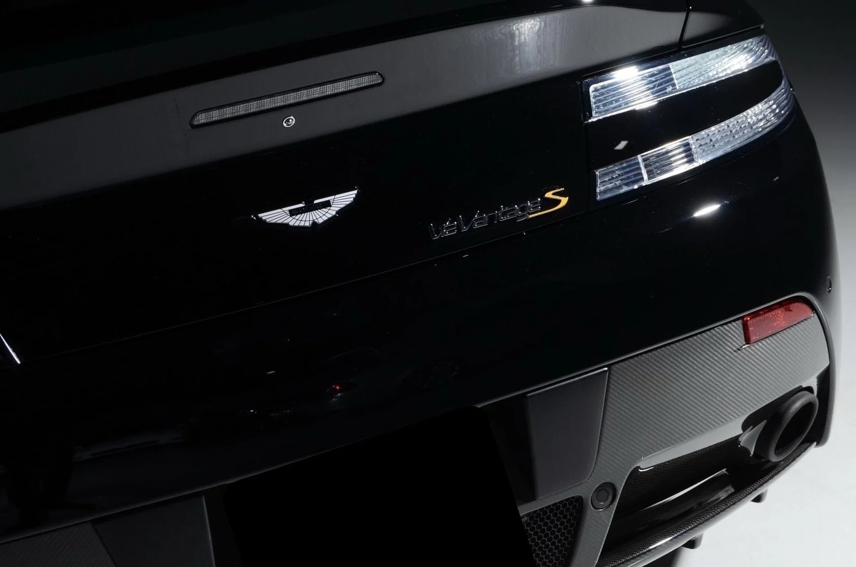 Close-up of the rear of a black Aston Martin Valhalla S sports car, showing the car's badge, taillights, and rear diffuser.