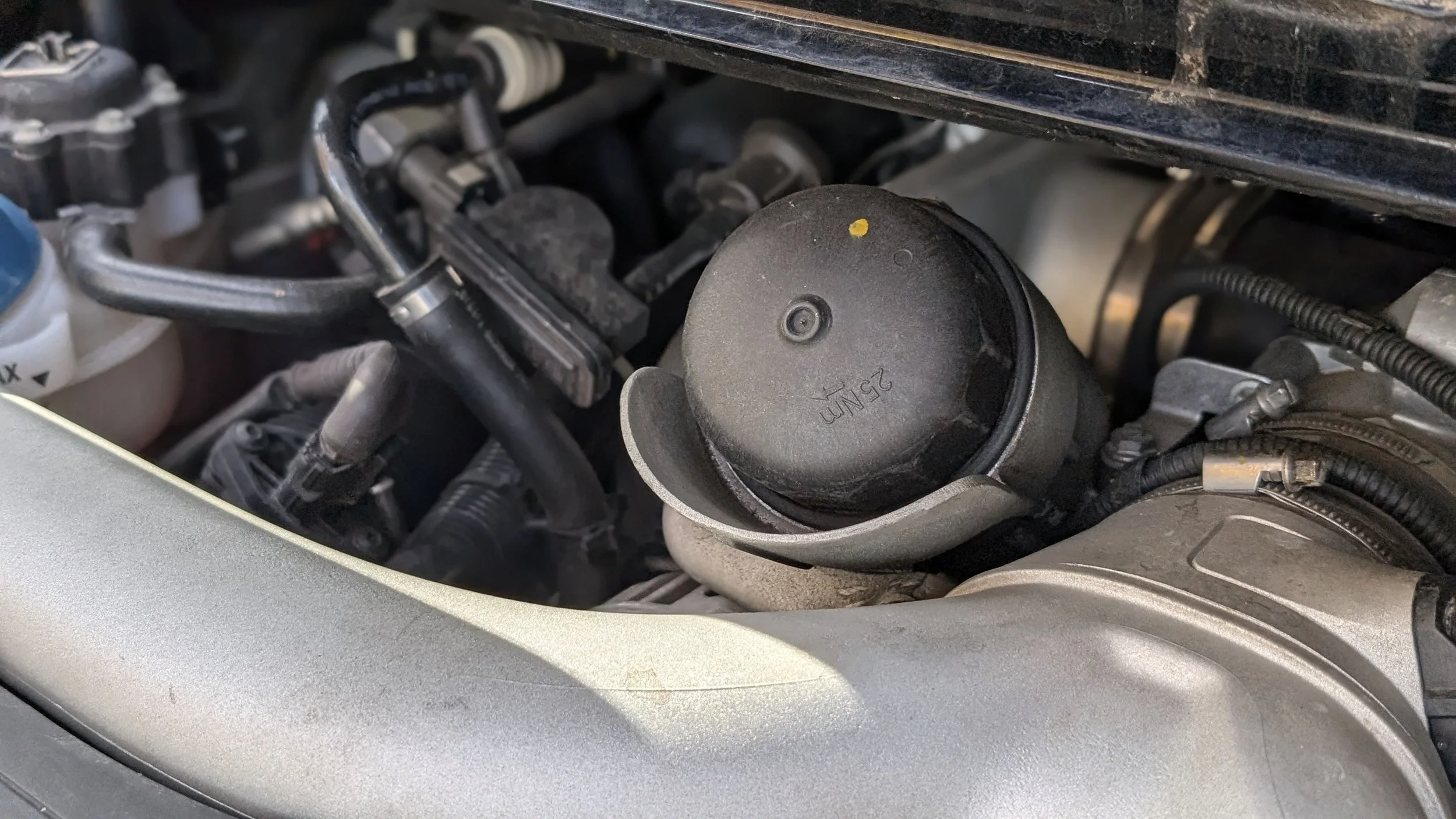Close-up of a car engine component, with a black cap marked 25 NM and surrounding hoses and mechanical parts.