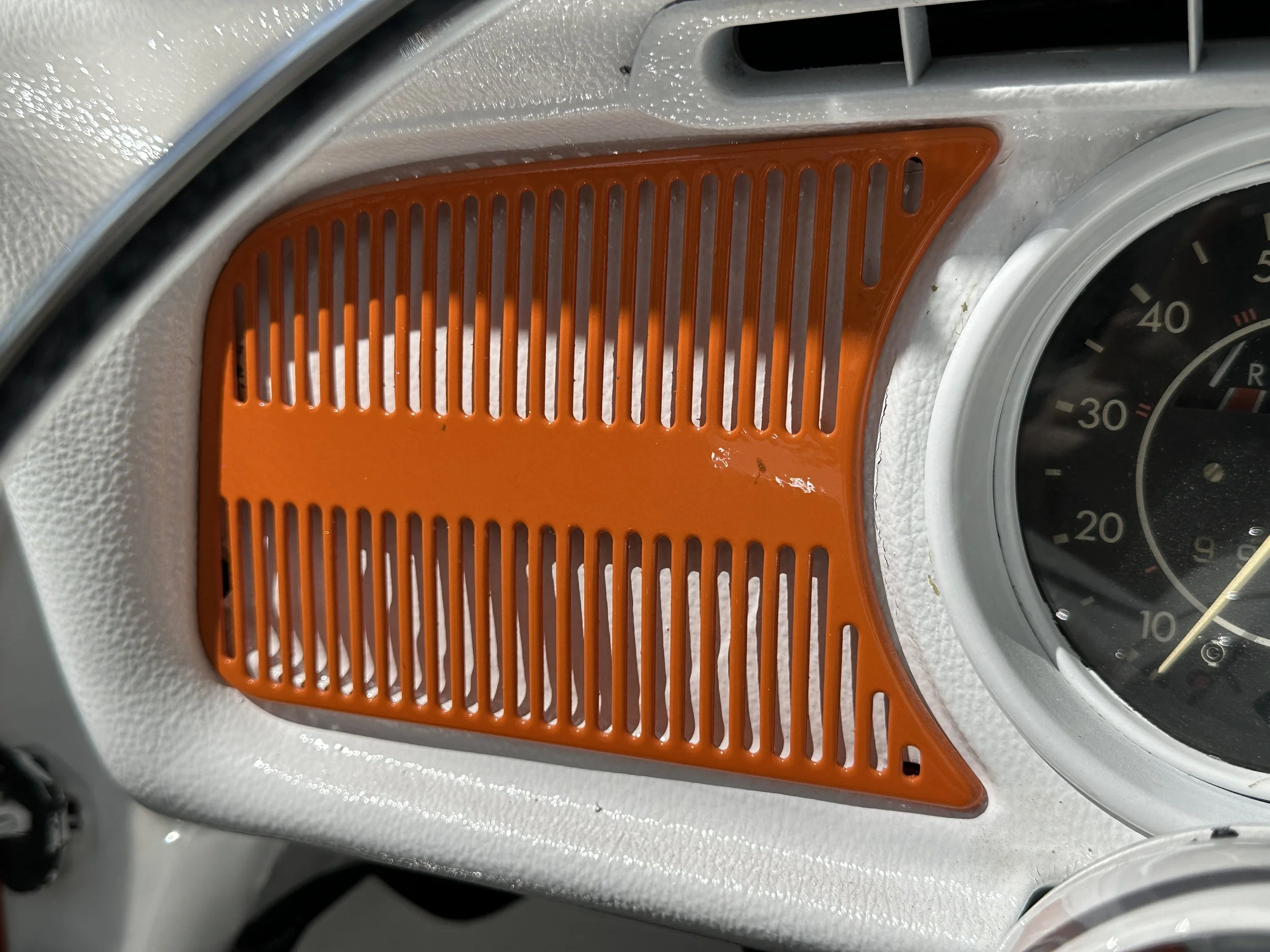 Close-up of a car dashboard with a speedometer and an orange vent cover.