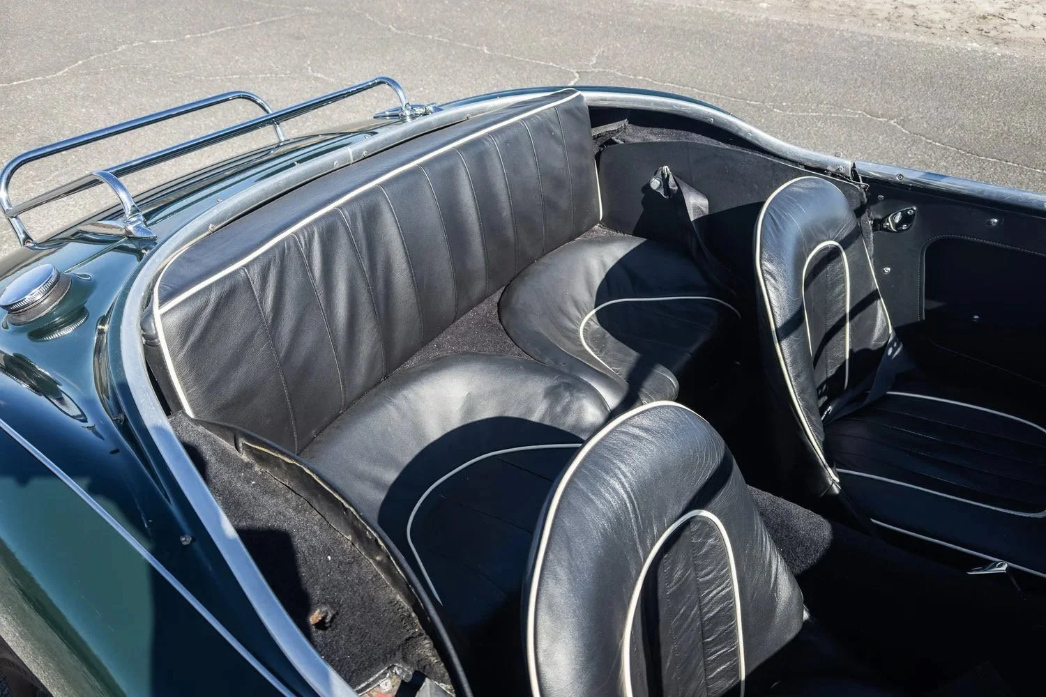 Interior of a vintage convertible car with black leather seats and a metal railing on the rear.