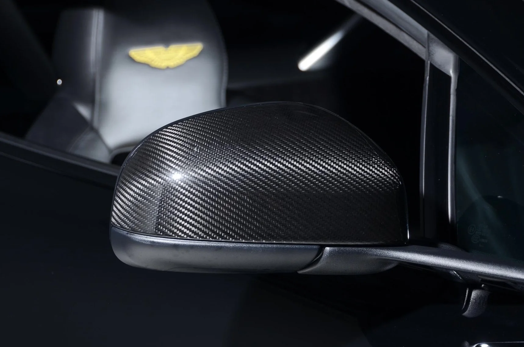 Close-up of a car's side mirror with a carbon fiber cover, reflecting part of the door and window.