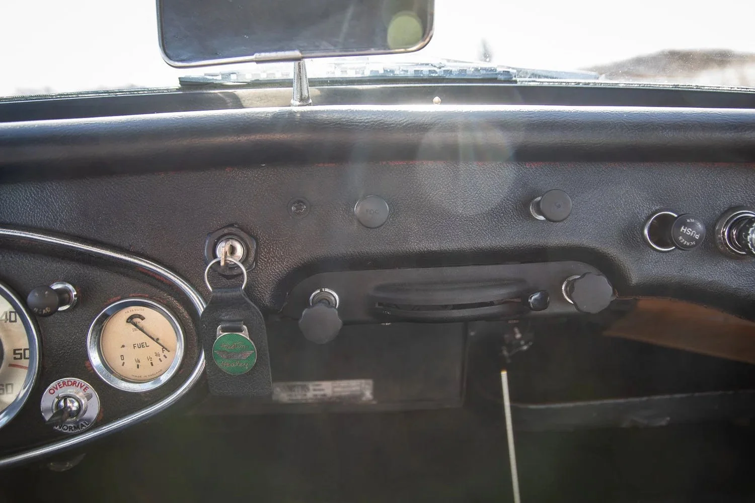 Dashboard of a vintage car with gauges, switches, and a key in the ignition.