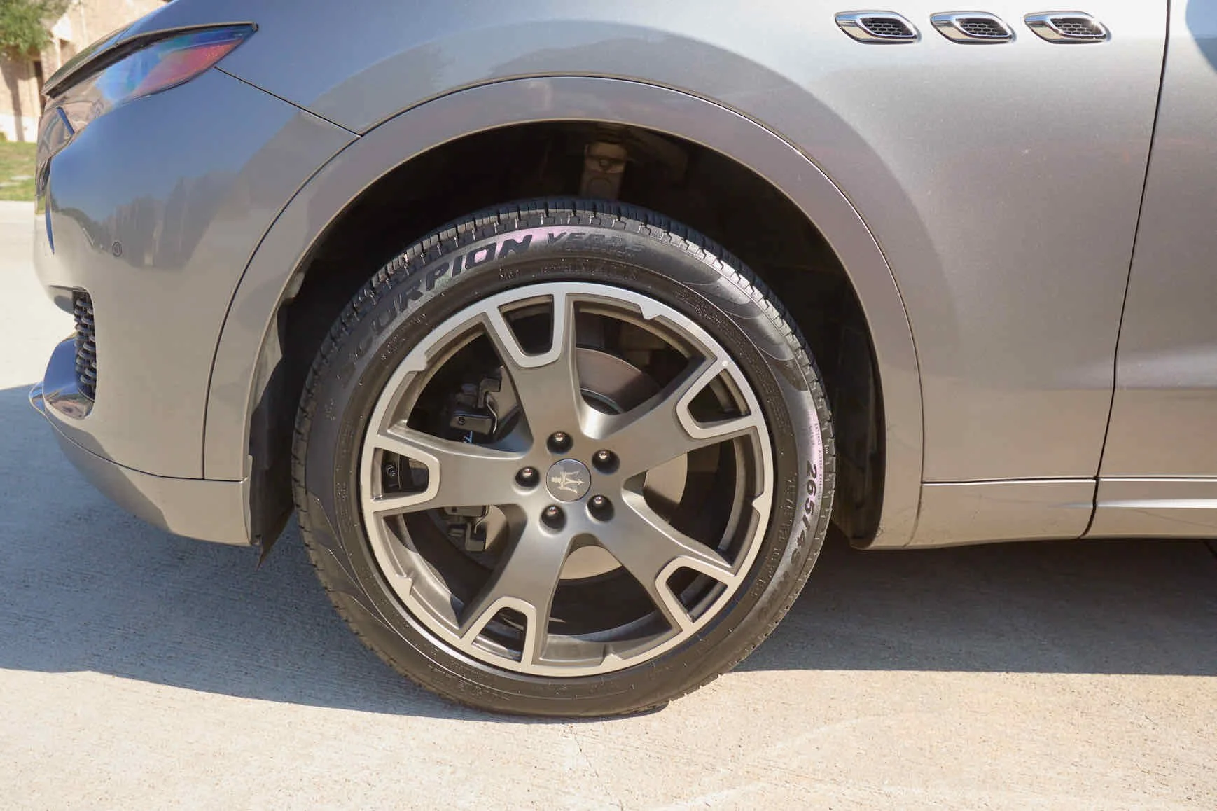 Close-up of a gray Maserati luxury car's front wheel and tire, parked on a concrete surface.