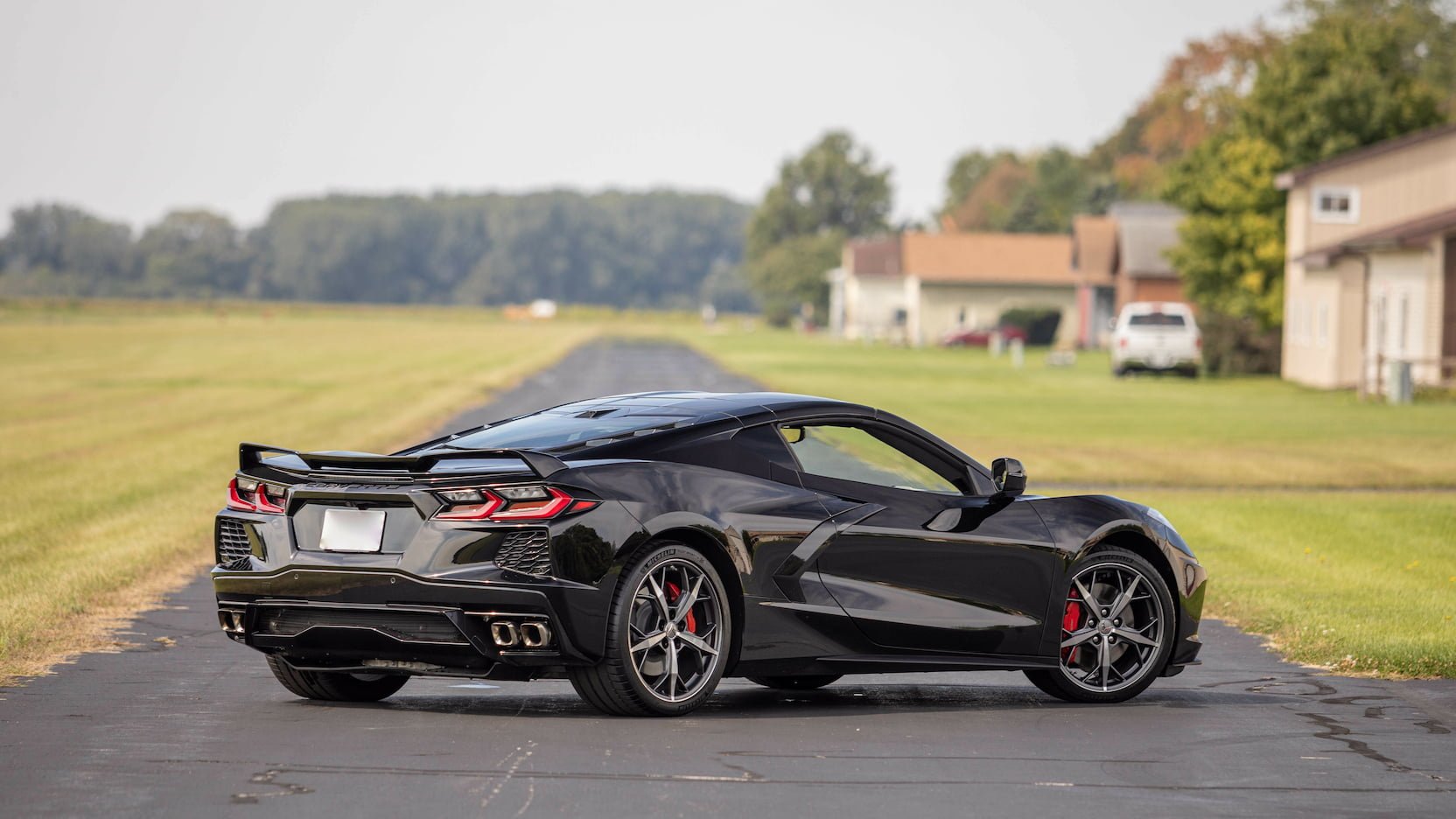 A black sports car parked on a driveway with houses and trees in the background.