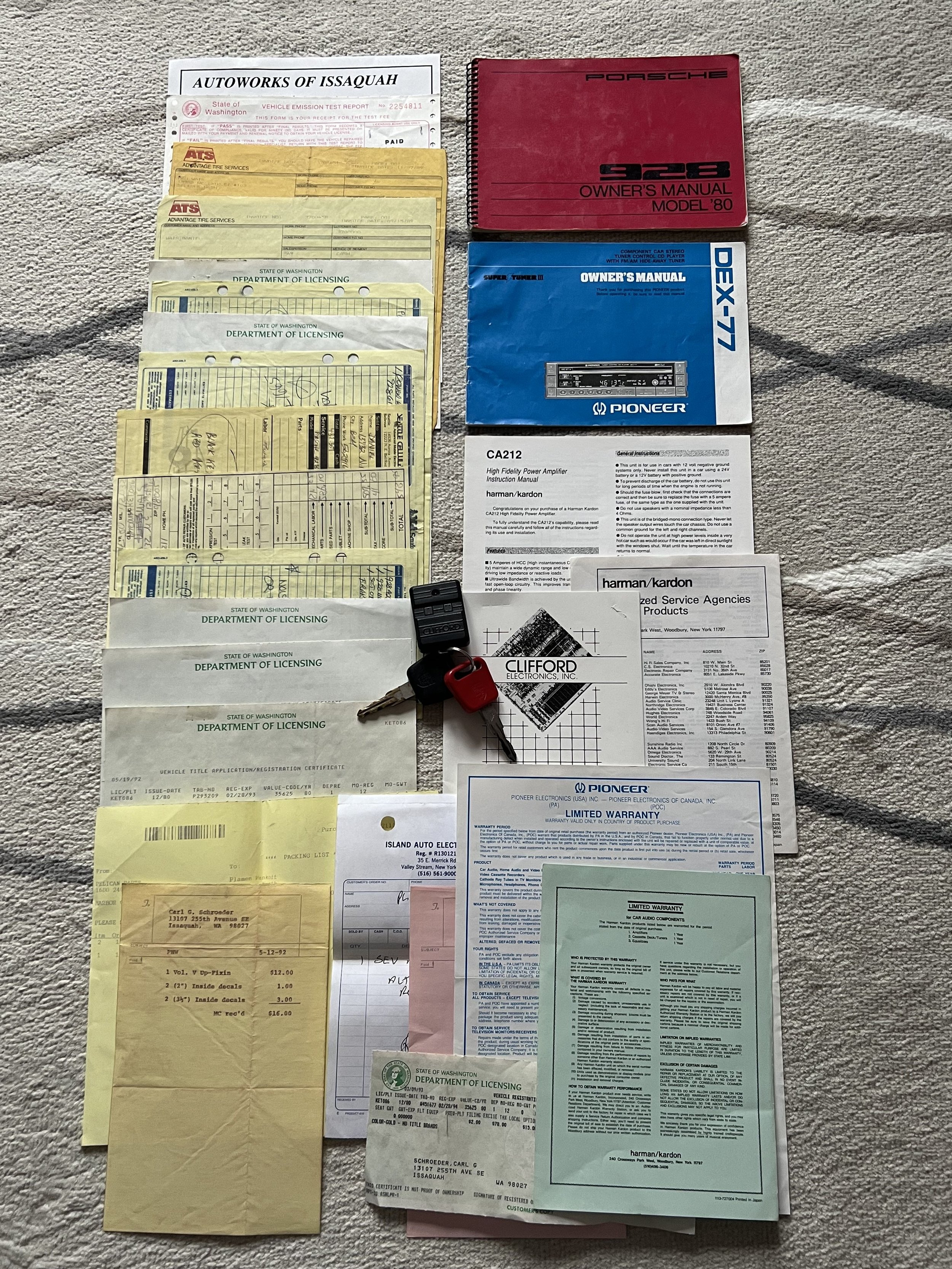 Collection of documents, manuals, receipts, and a car key with a key fob arranged on a carpeted surface.