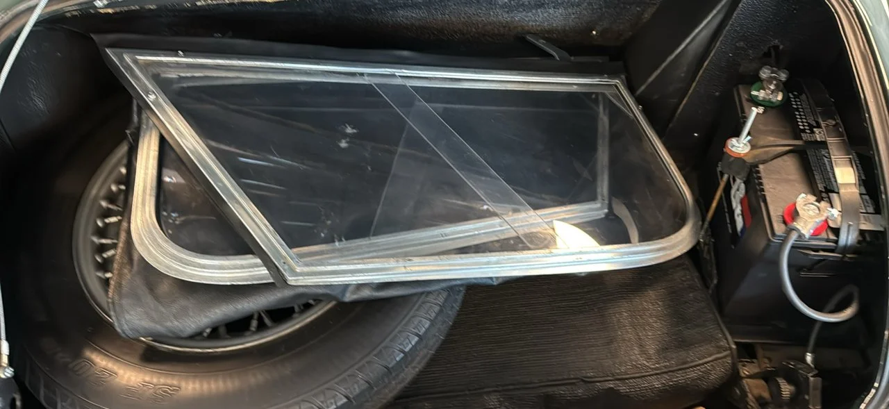 Spare tire, large plastic container, and car battery inside a vehicle trunk.