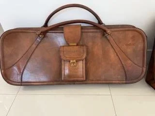 A vintage brown leather Schedoni Ferrari 512 suitcase with a handle, small front pocket, and zippered compartments, placed on a tiled floor.