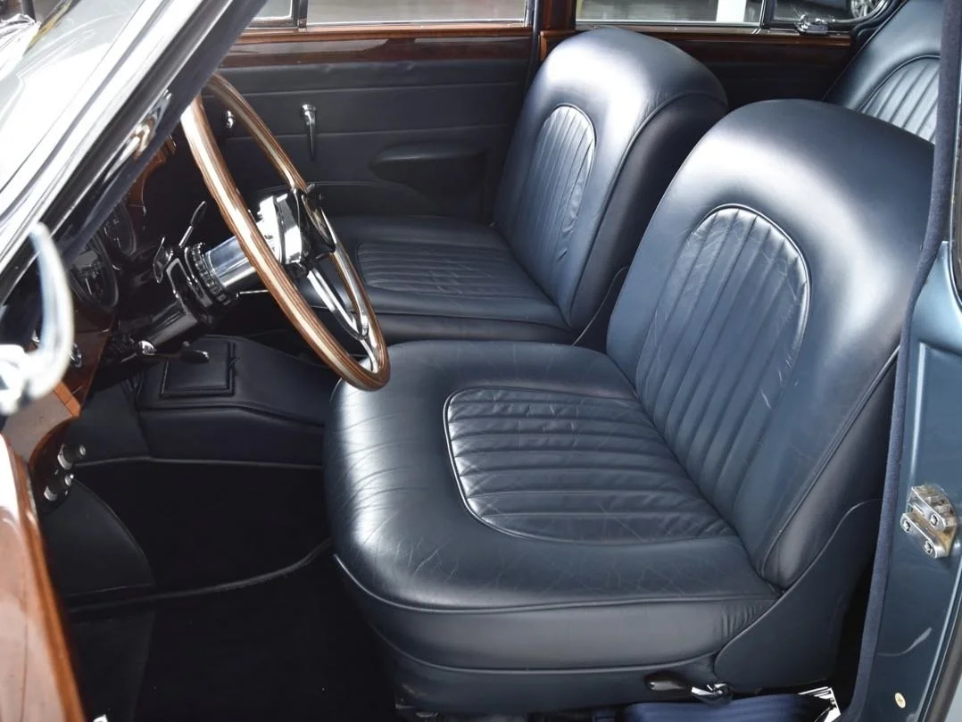 Interior of a vintage car with black leather seats, wooden dashboard, and steering wheel.