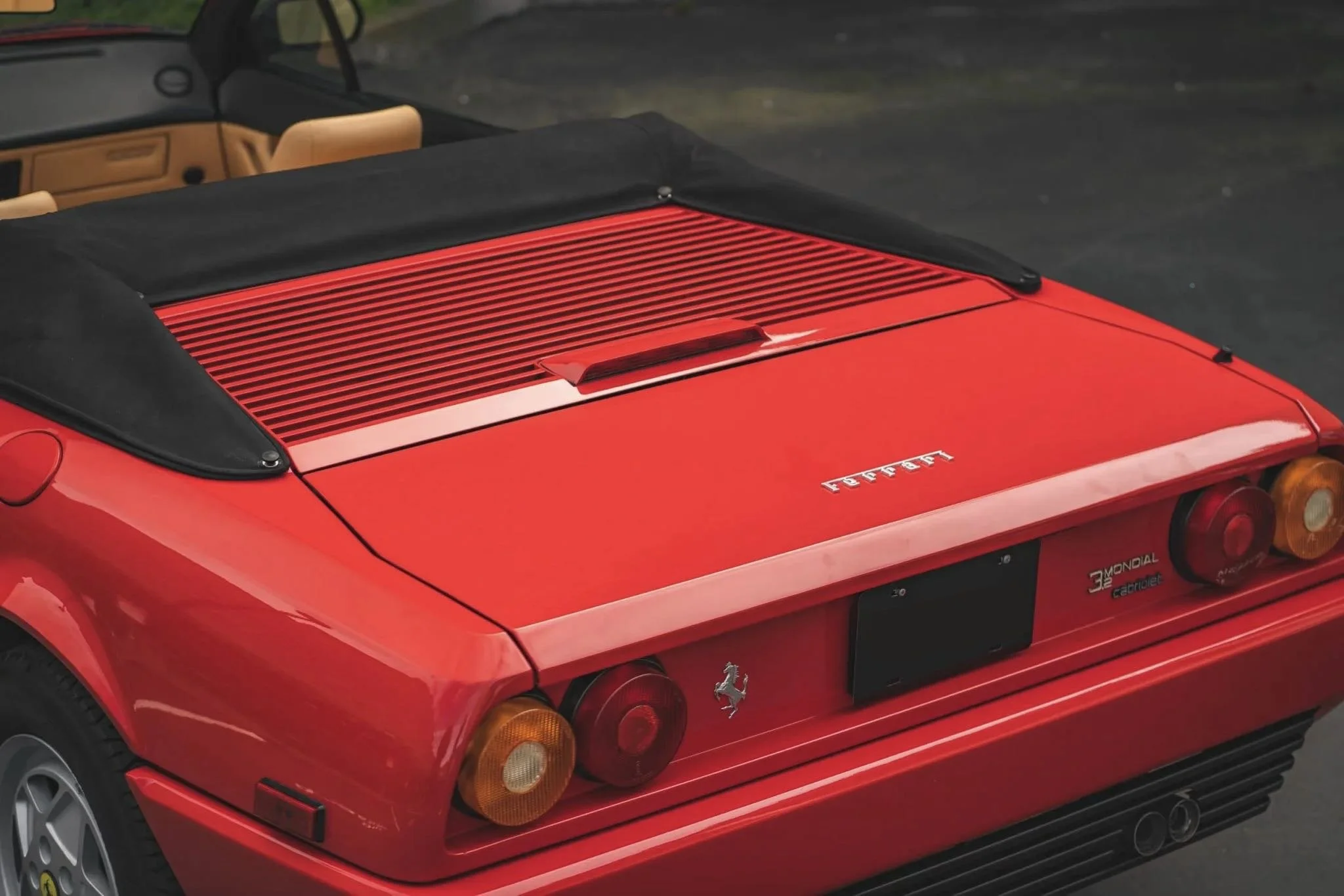 Rear view of a red Ferrari sports car with a black convertible top, showing the Ferrari logo, tail lights, and dual exhaust pipes.