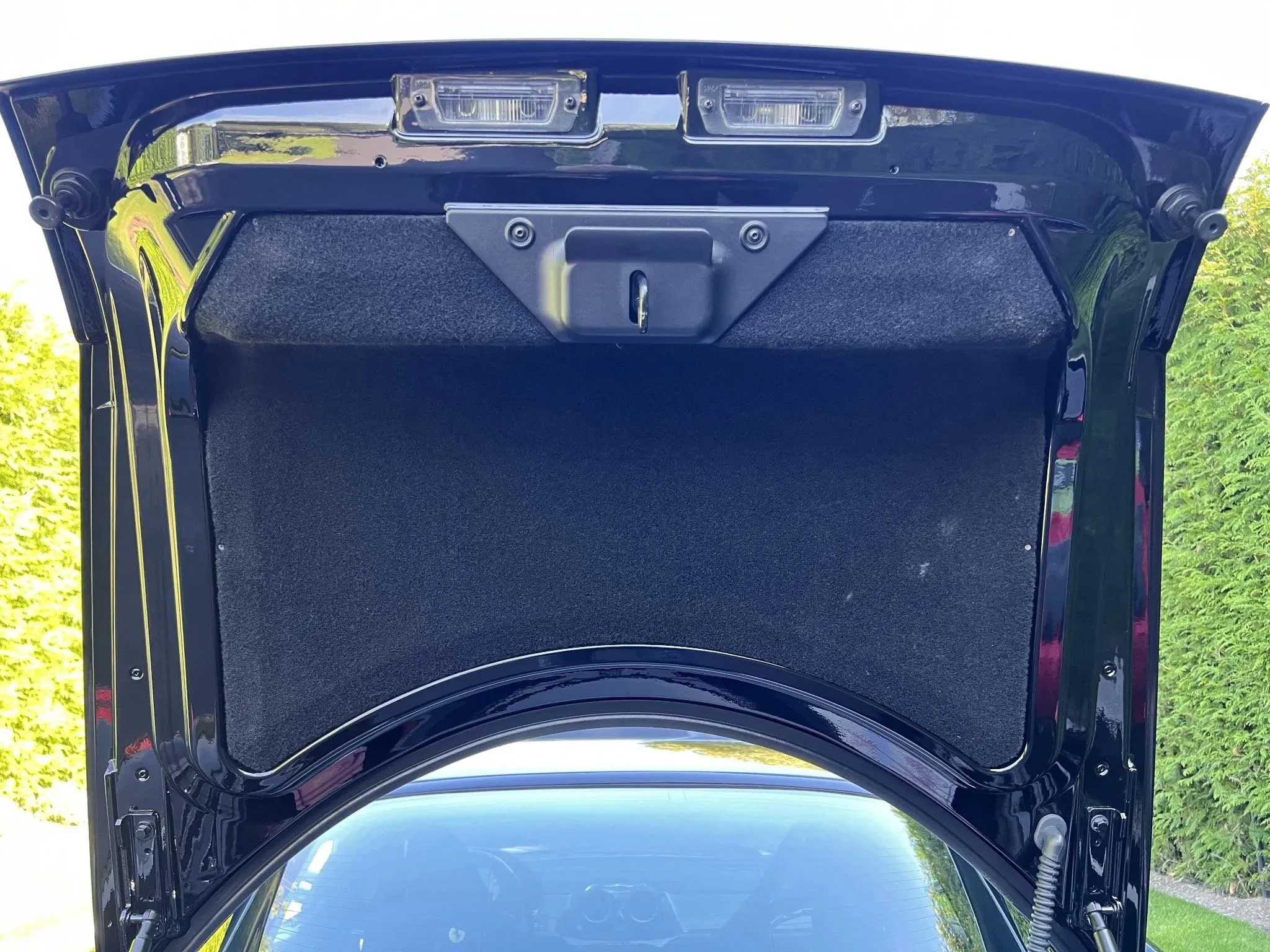 Open car trunk showing a black carpeted interior with a latch and lights inside the trunk lid.