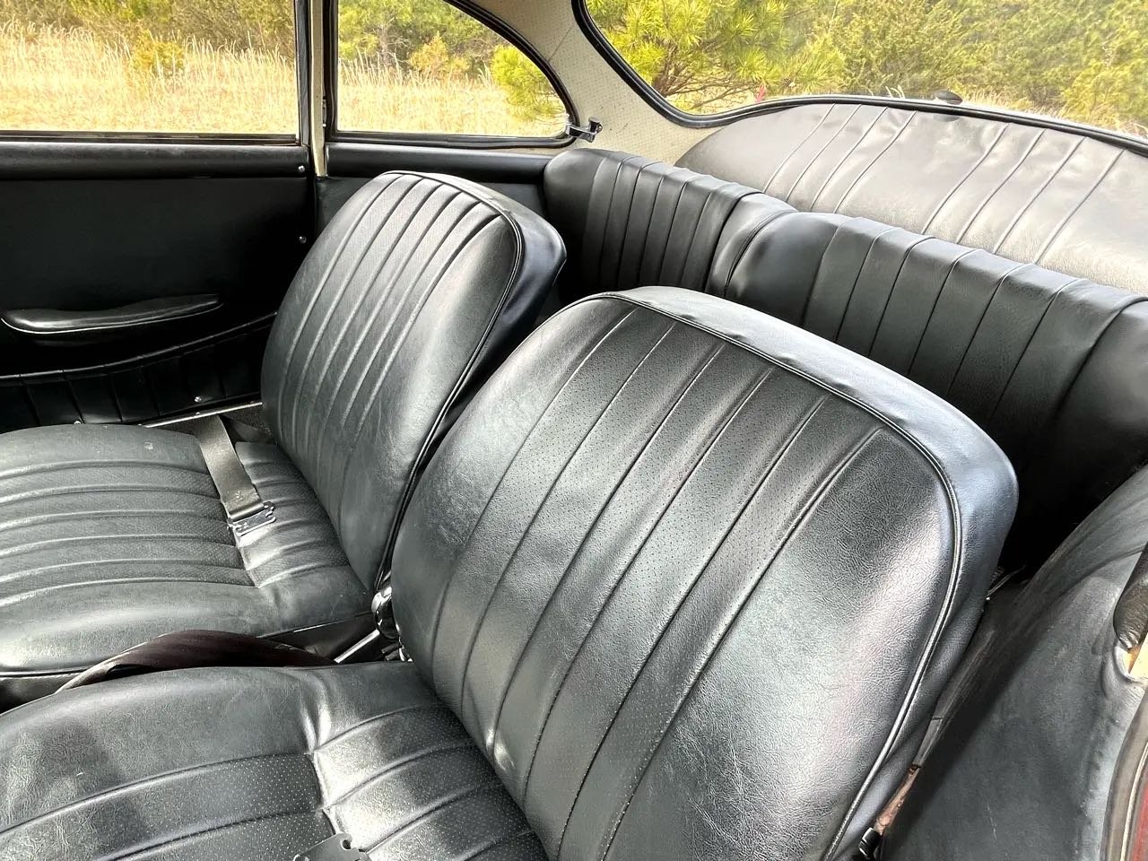 Interior of a vintage car with black leather bench seats and side panels, showing the front and back seats and windows.
