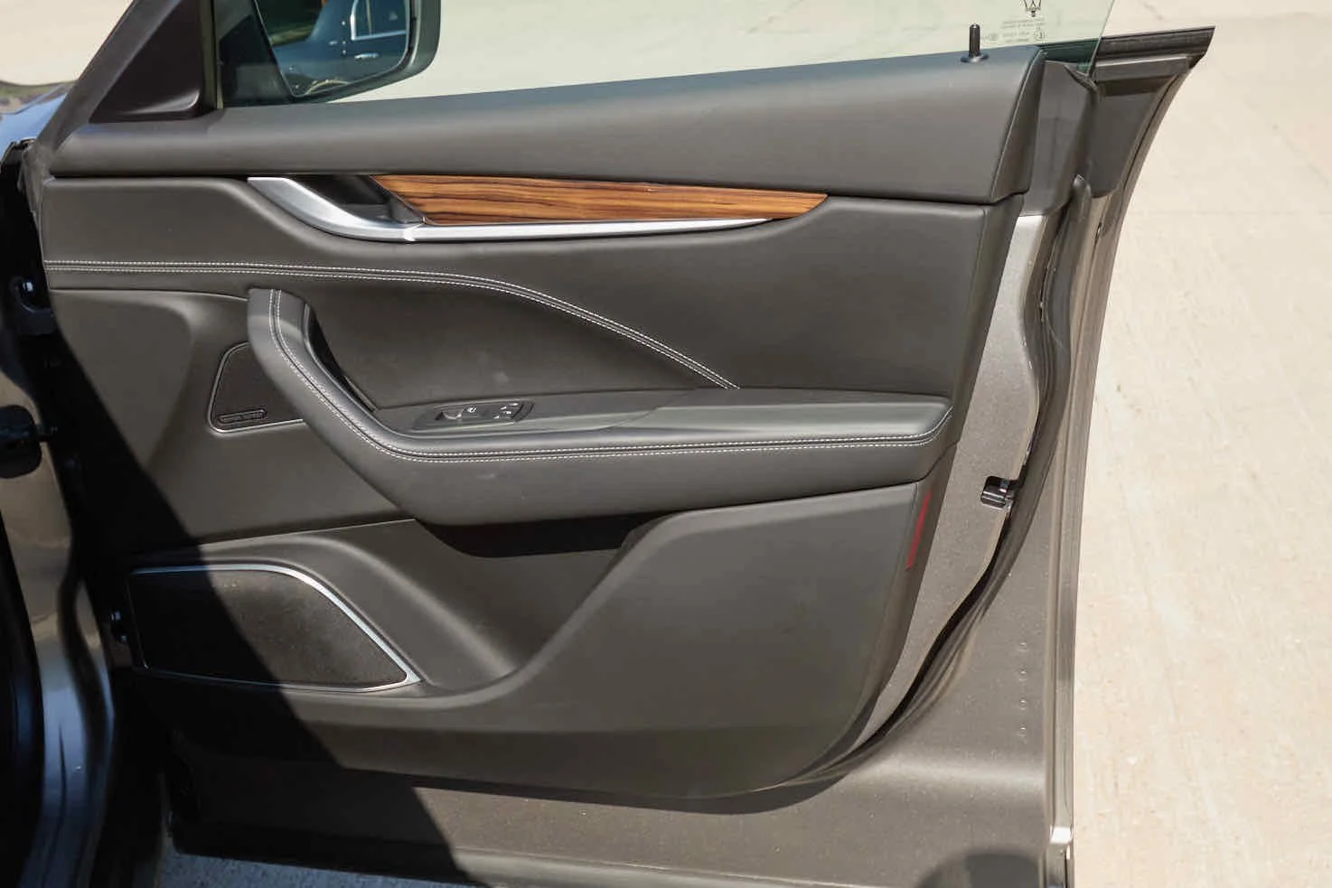 Inside view of a car door with gray leather, wood trim, and chrome accents.