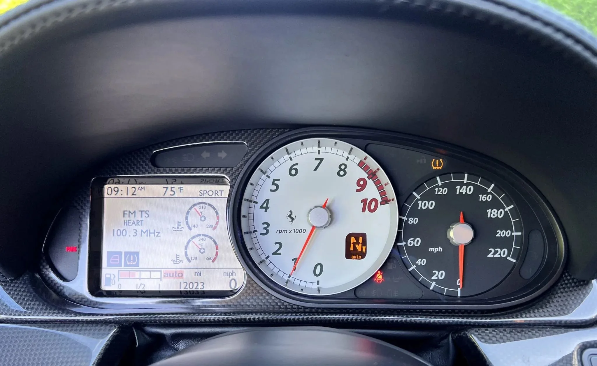 Close-up of a car dashboard showing a digital display with radio information, a tachometer, and a speedometer. Warning lights for tire pressure and seatbelt.