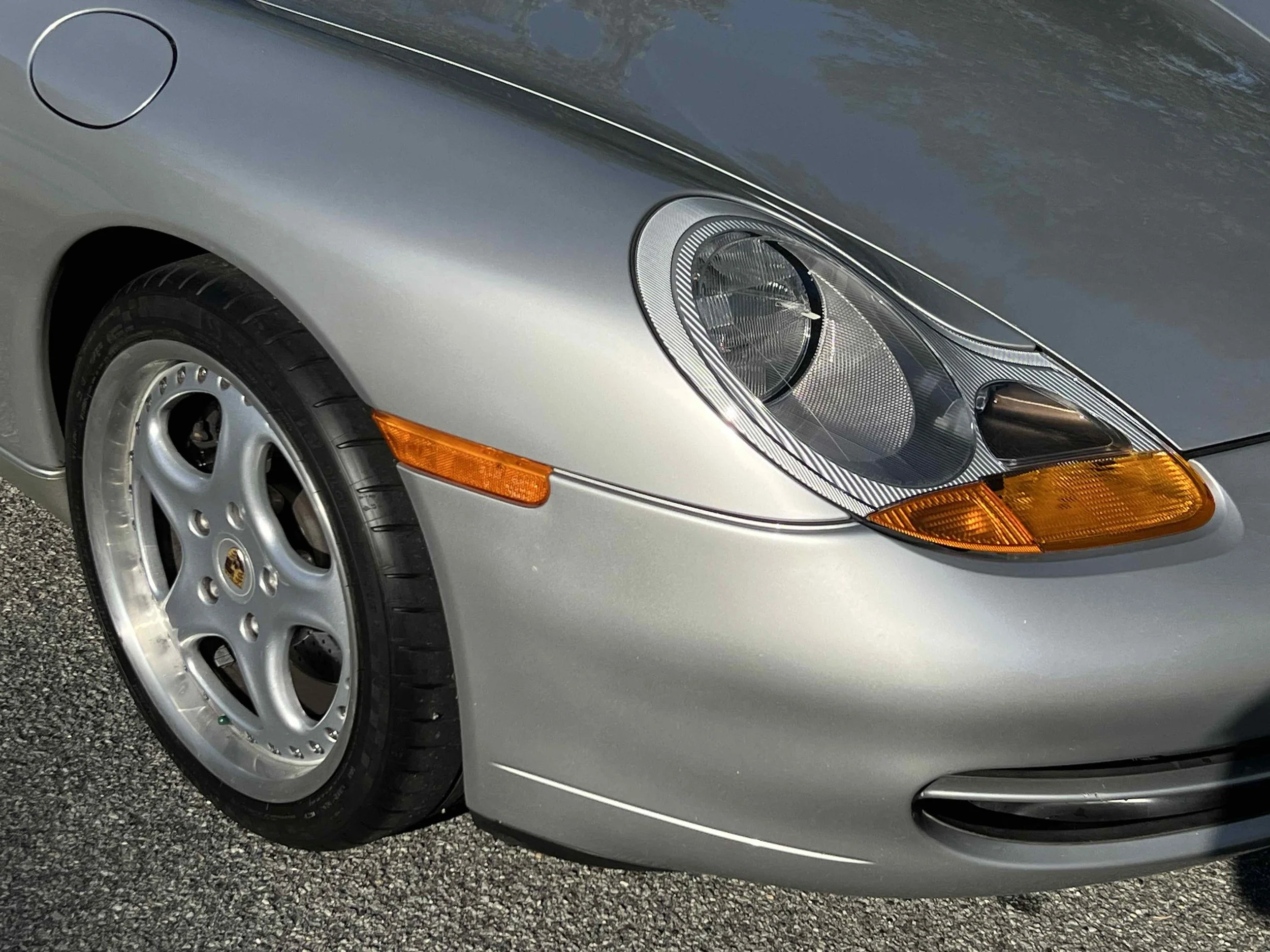 Close-up of the front part of a silver Porsche sports car showing its headlight, wheel, and front bumper.