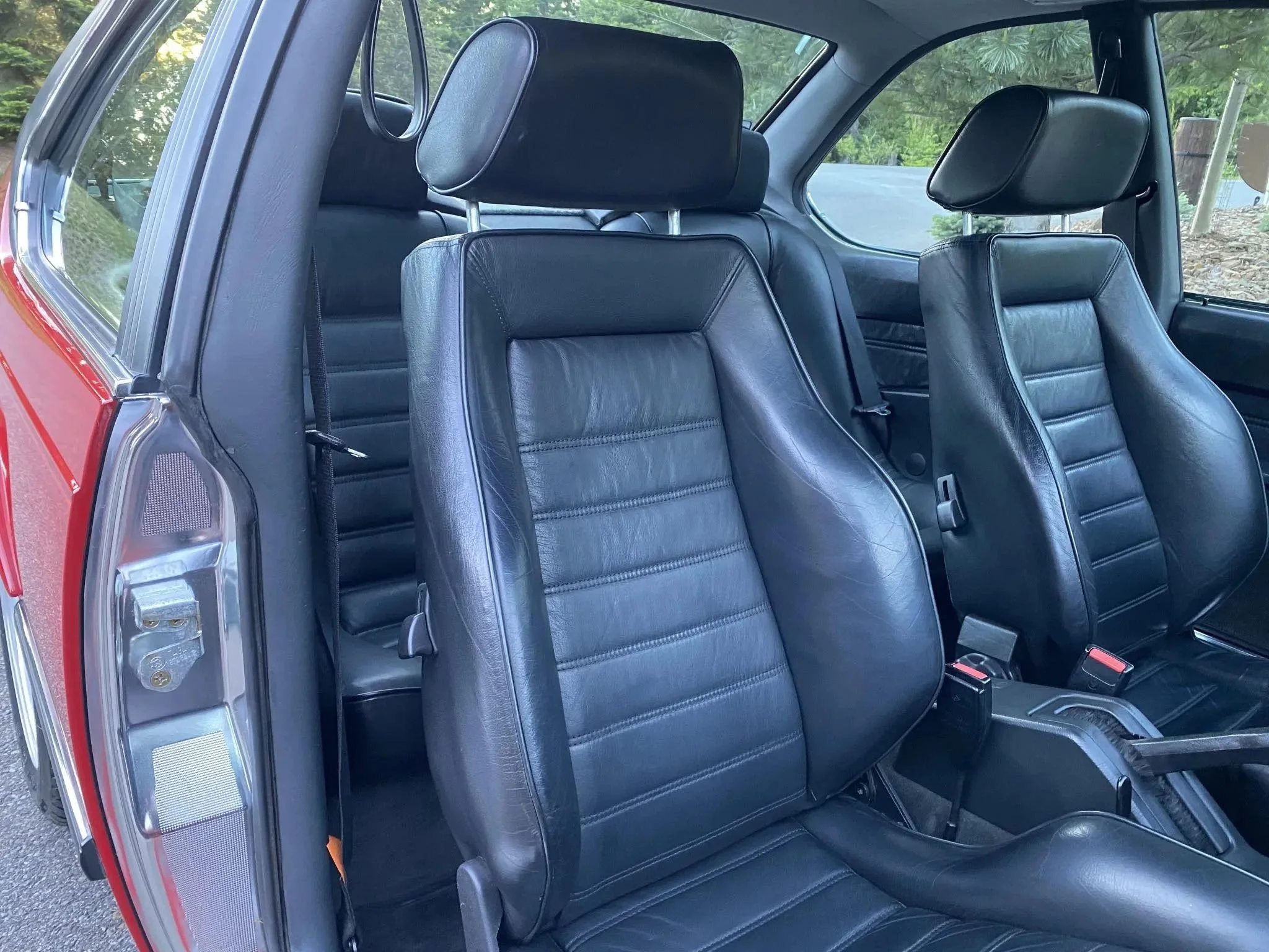 Inside a car showing black leather front and rear seats with headrests, and partially visible steering wheel, dashboard, and door.