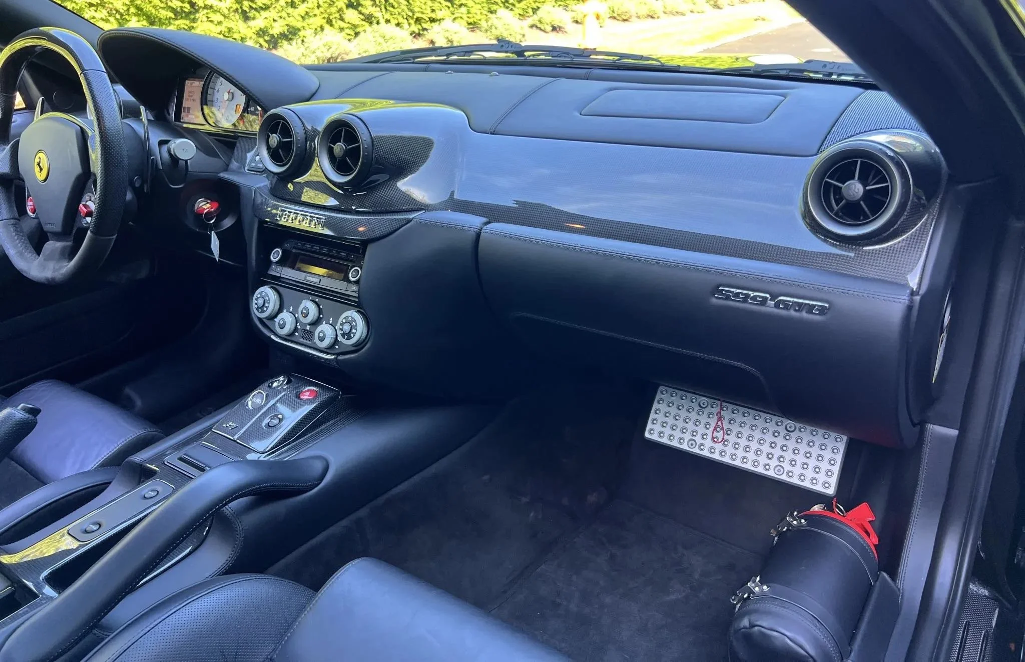 Interior of a Ferrari sports car with black leather seats, carbon fiber dashboard, and sporty controls, including dual air vents and a gear shift.