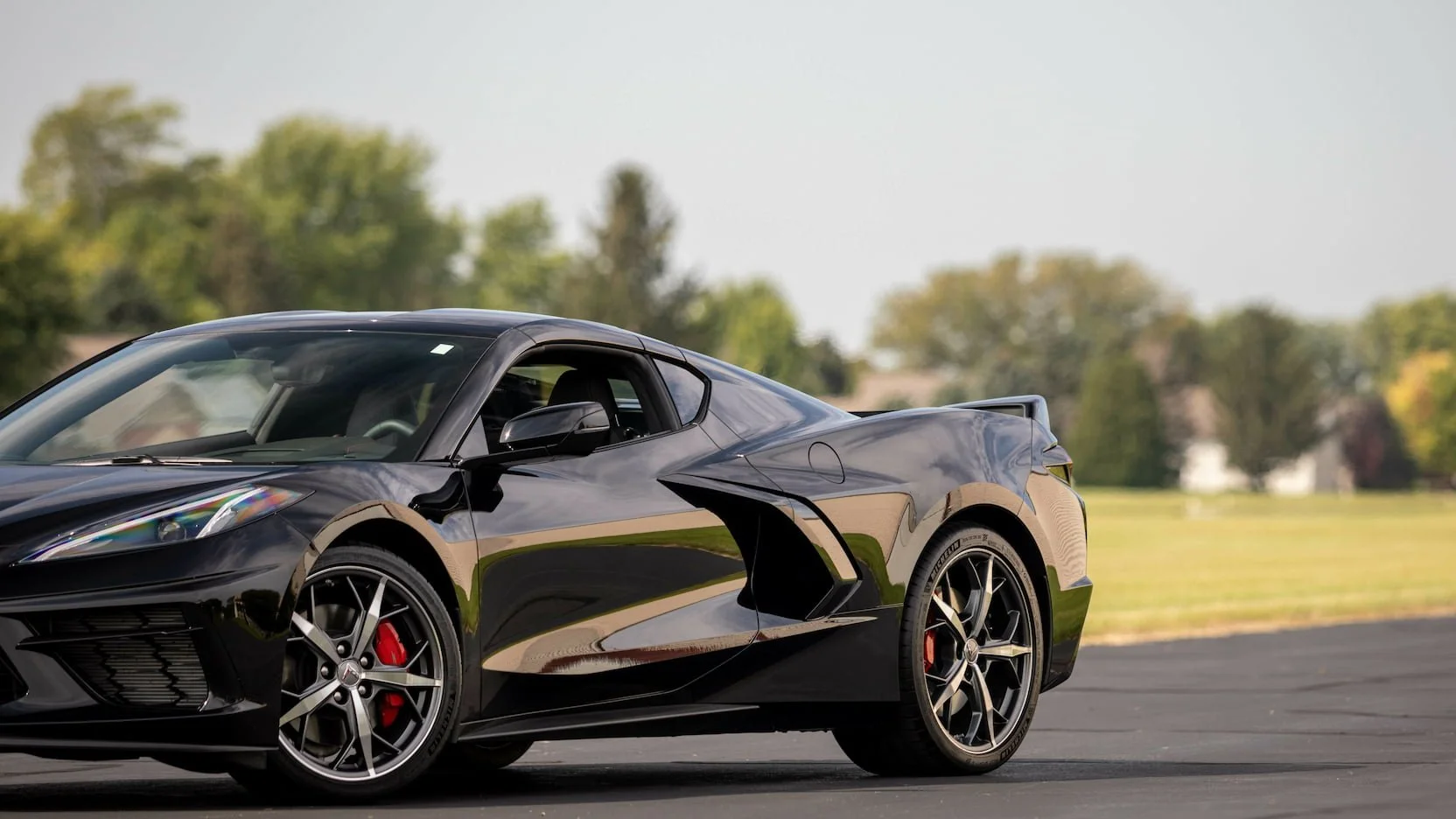 Black sports car parked on a paved surface with trees and grass in the background