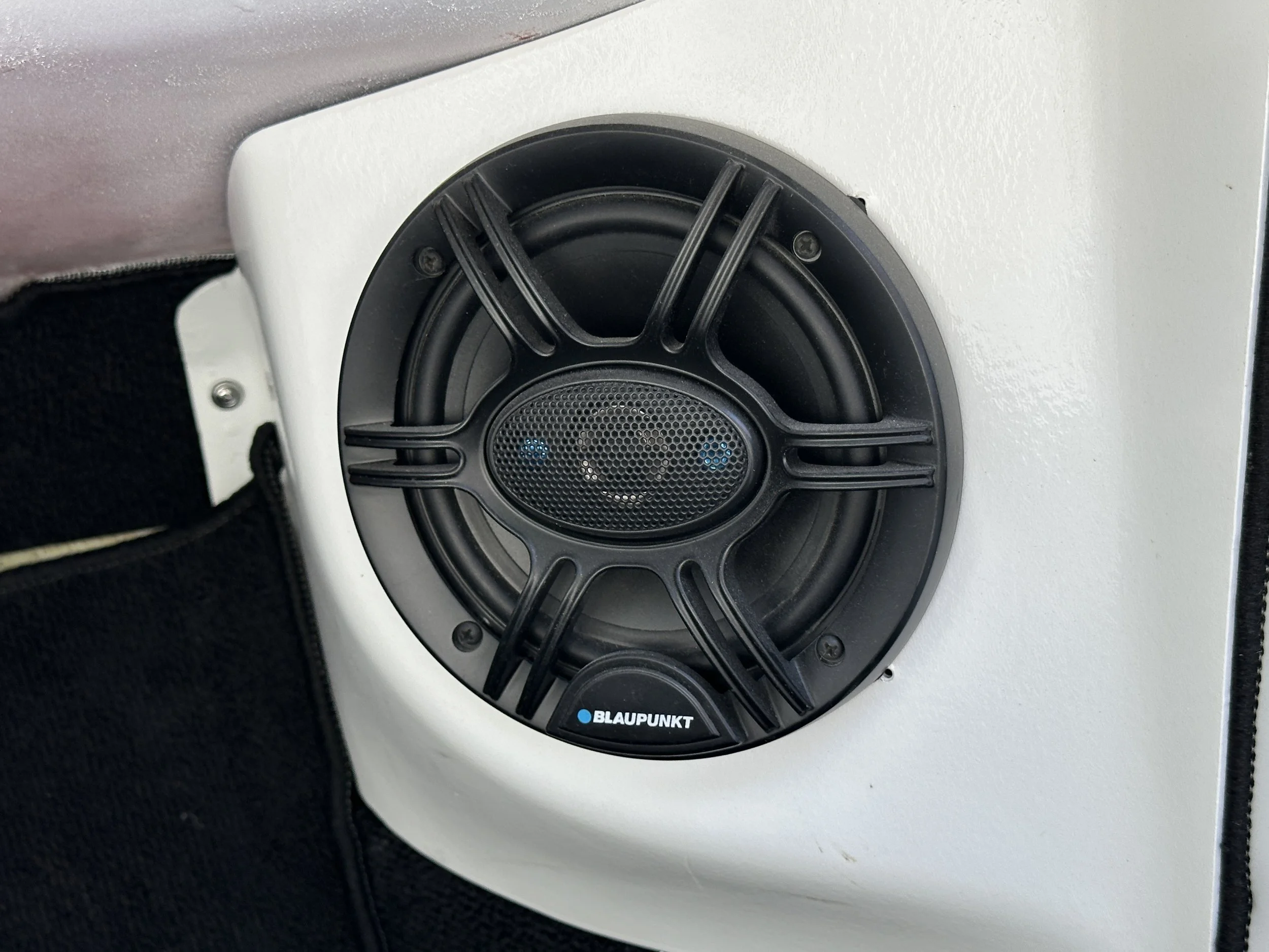 A Blaupunkt speaker mounted on a white surface, surrounded by black fabric.