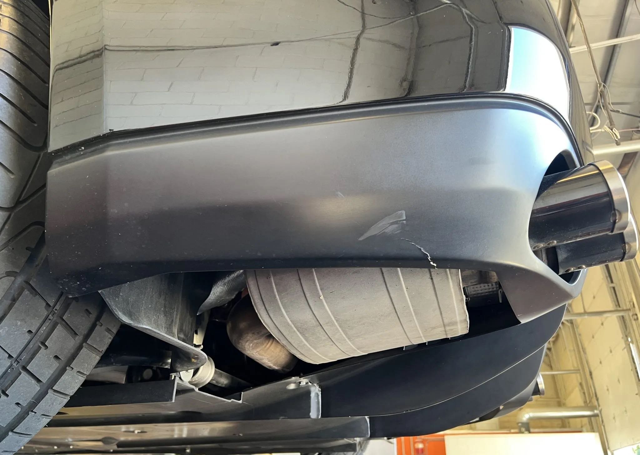 Close-up of the front right side of a black car, showing the front bumper, part of the tire, and the exhaust pipe.